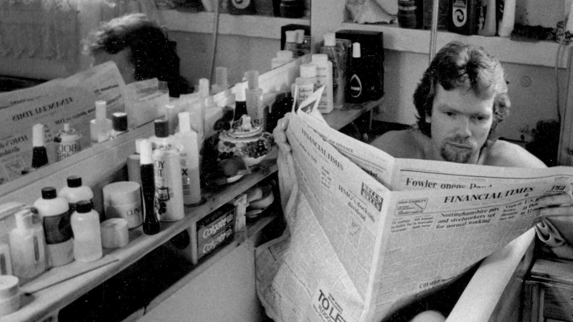 A Man Reading A Newspaper In A Bathroom