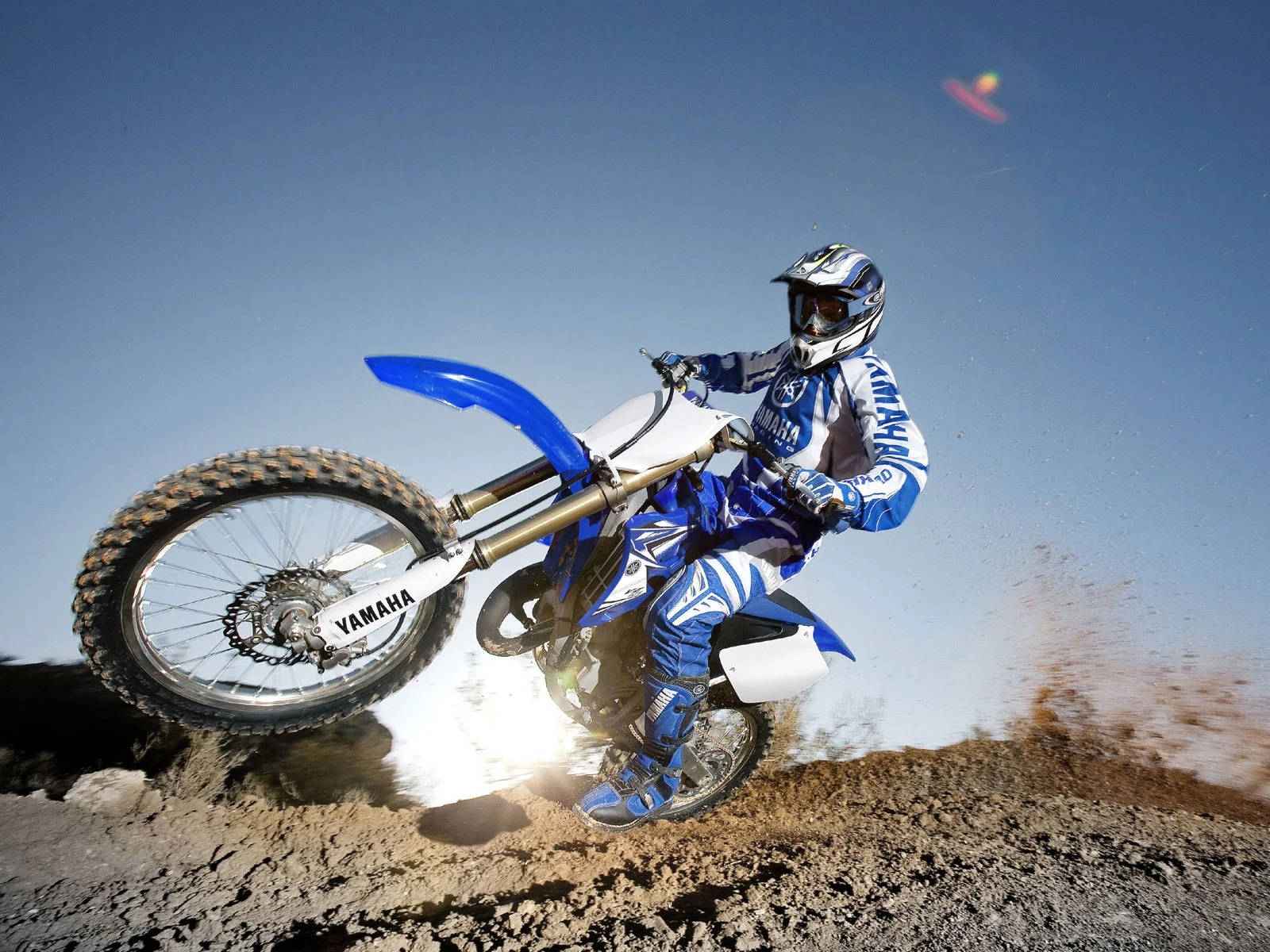 A Man Riding A Blue Dirt Bike On A Dirt Track Background