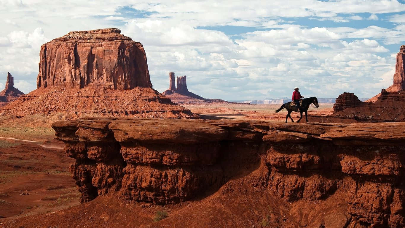 A Man Riding A Horse On A Cliff In Monument Valley Background