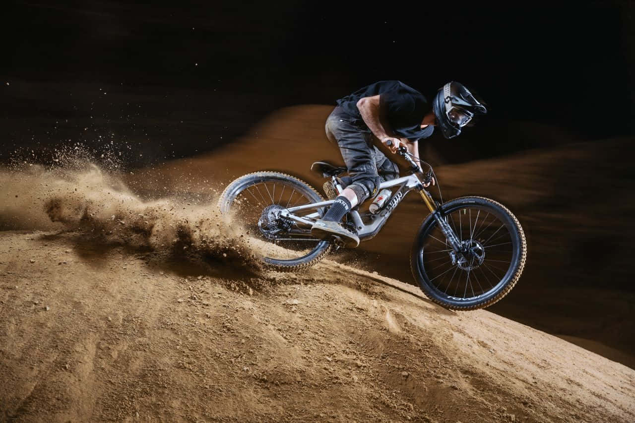 A Man Riding A Mountain Bike On A Dirt Hill Background