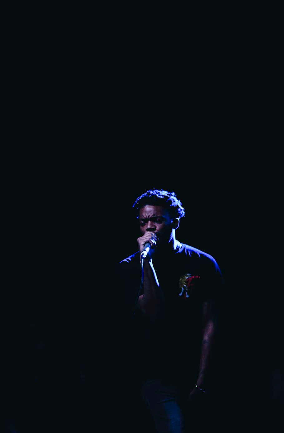 A Man Singing Into A Microphone In The Dark Background