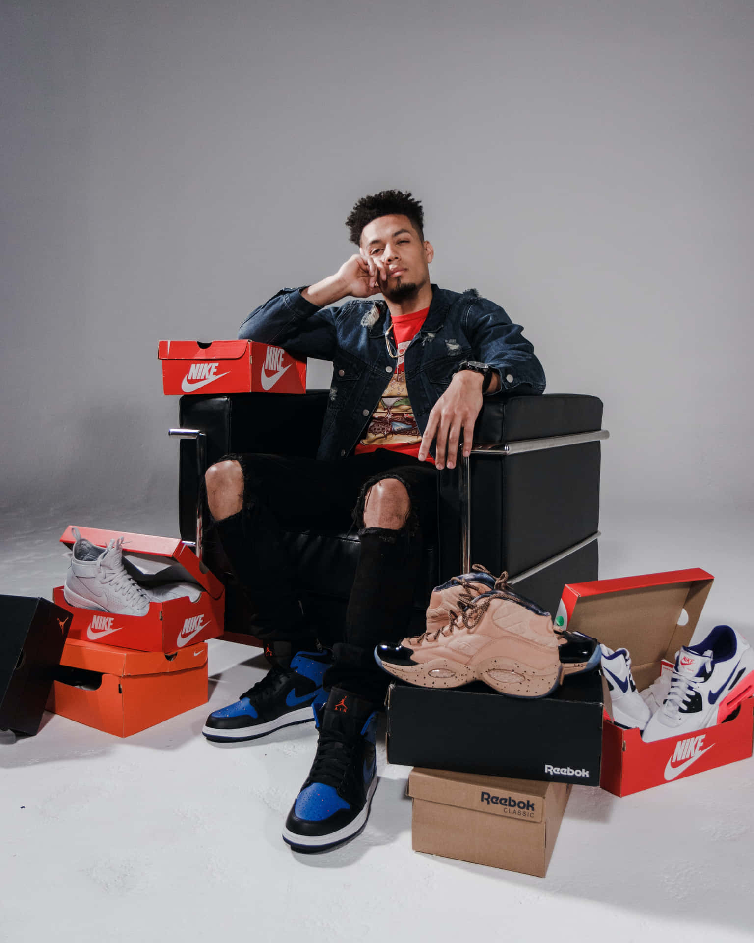 A Man Sitting In A Chair With A Lot Of Shoes Background