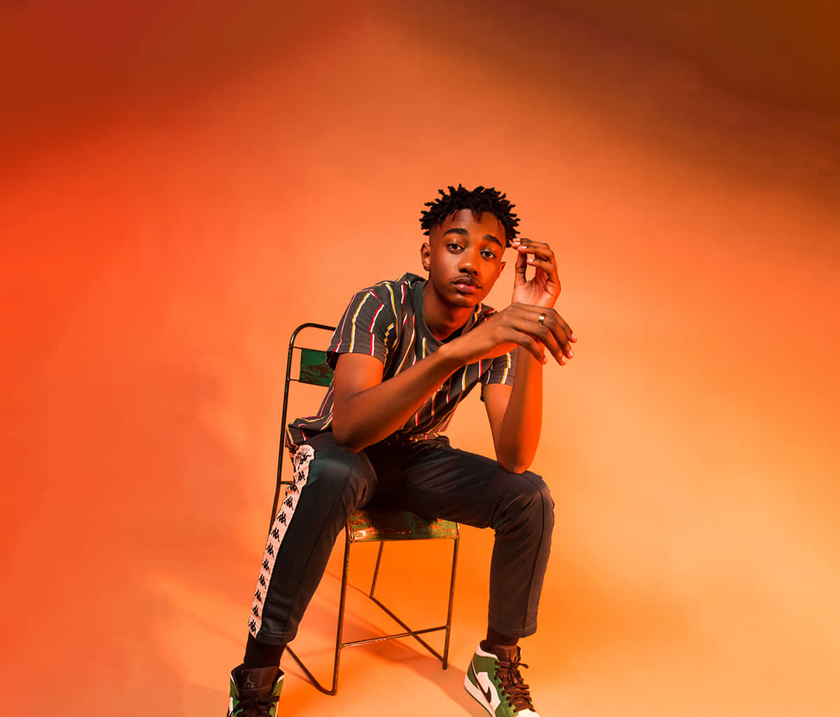 A Man Sitting On A Chair With His Hands On His Hips Background