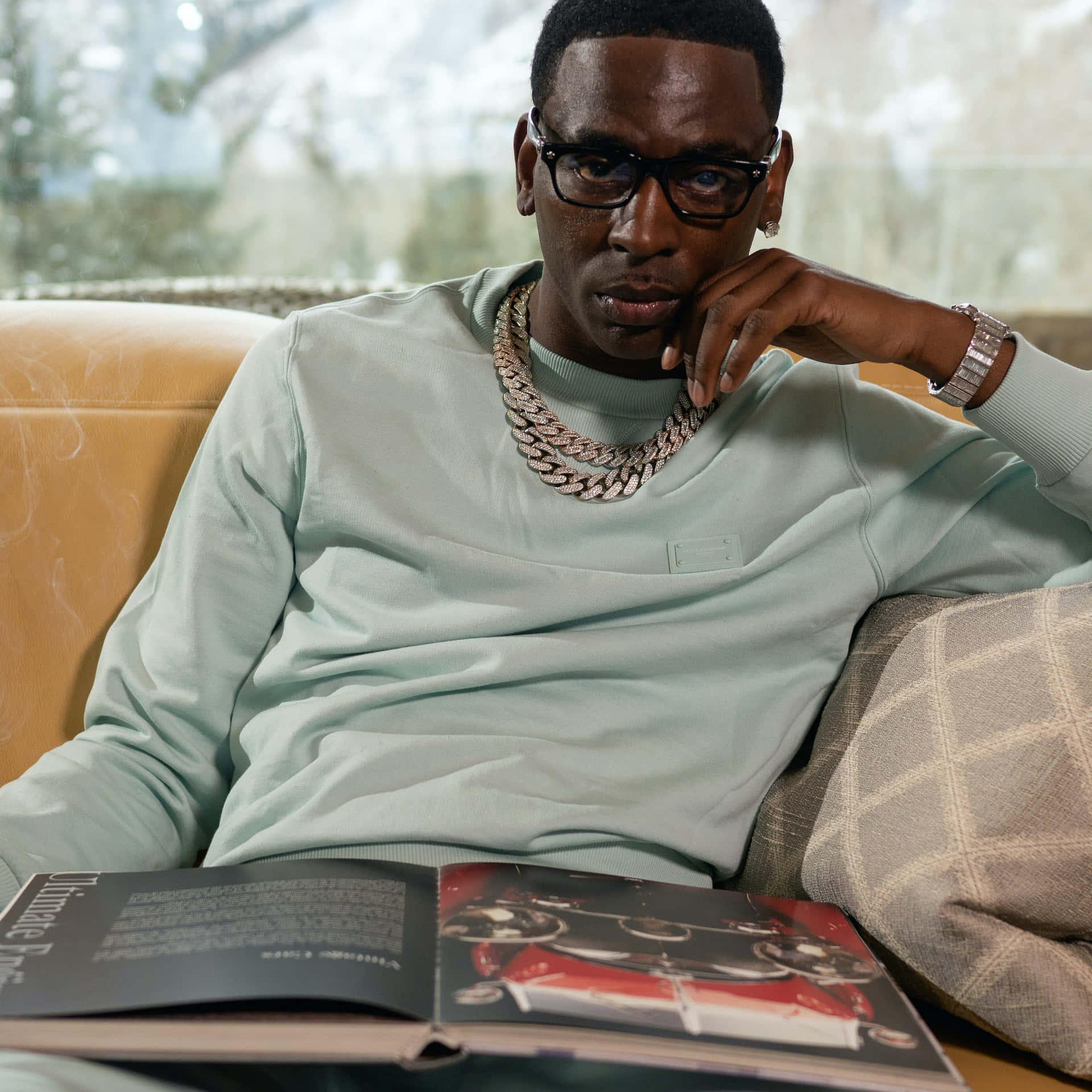 A Man Sitting On A Couch With A Book Background