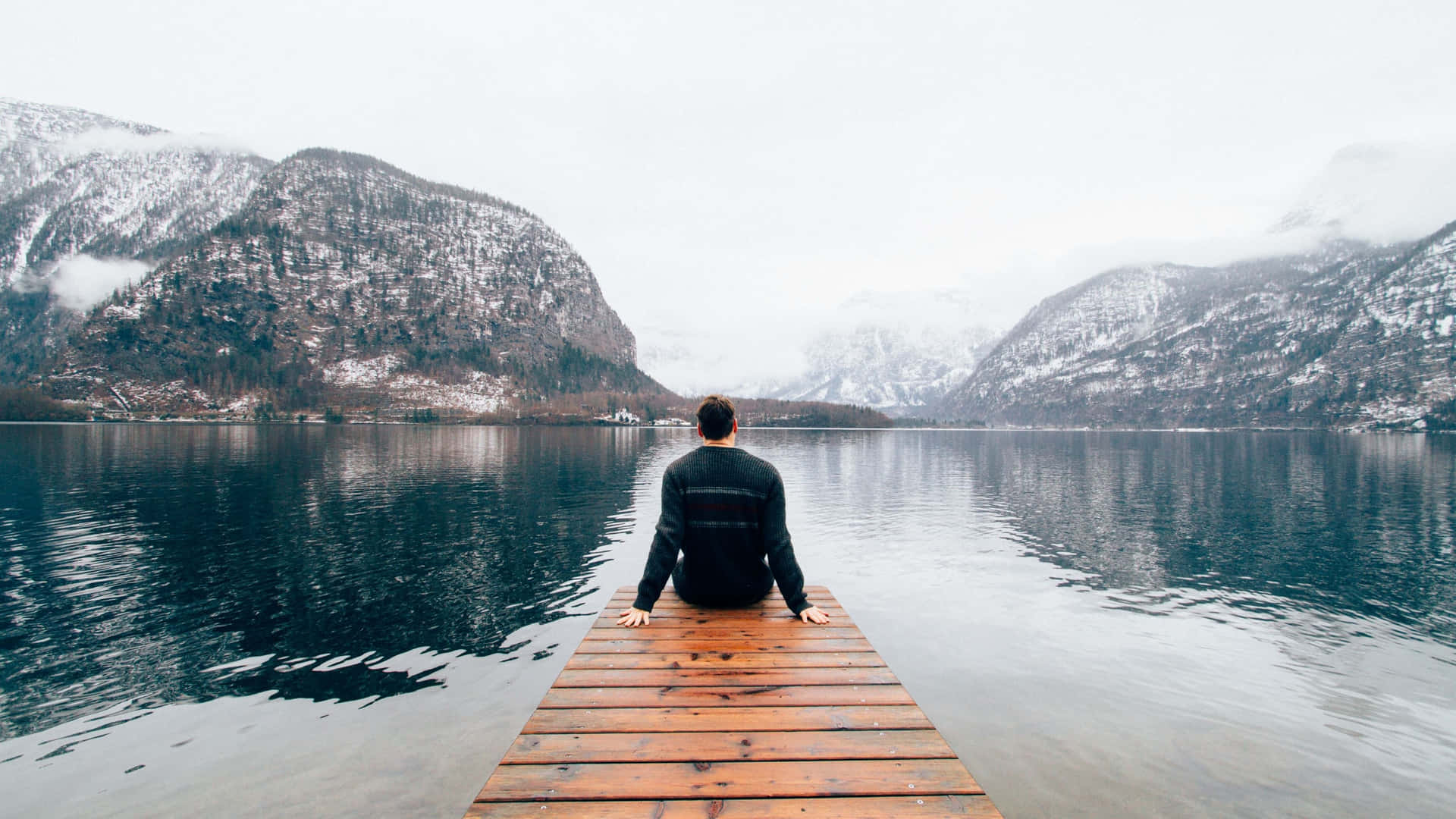 A Man Sitting On A Dock In The Snow Background