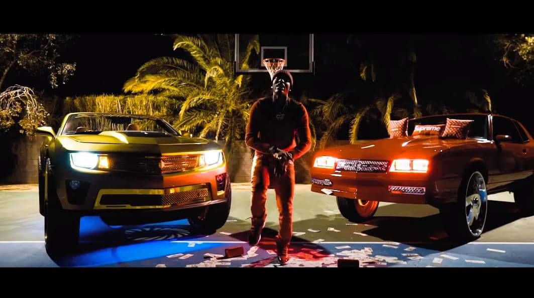 A Man Standing Next To Two Cars With Lights On Background