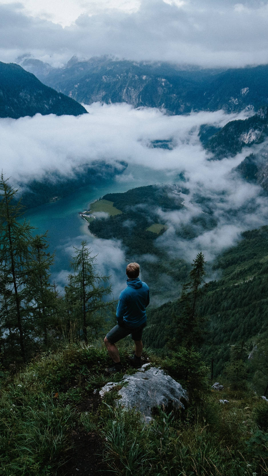 A Man Standing On A Mountain Overlooking A Lake Background