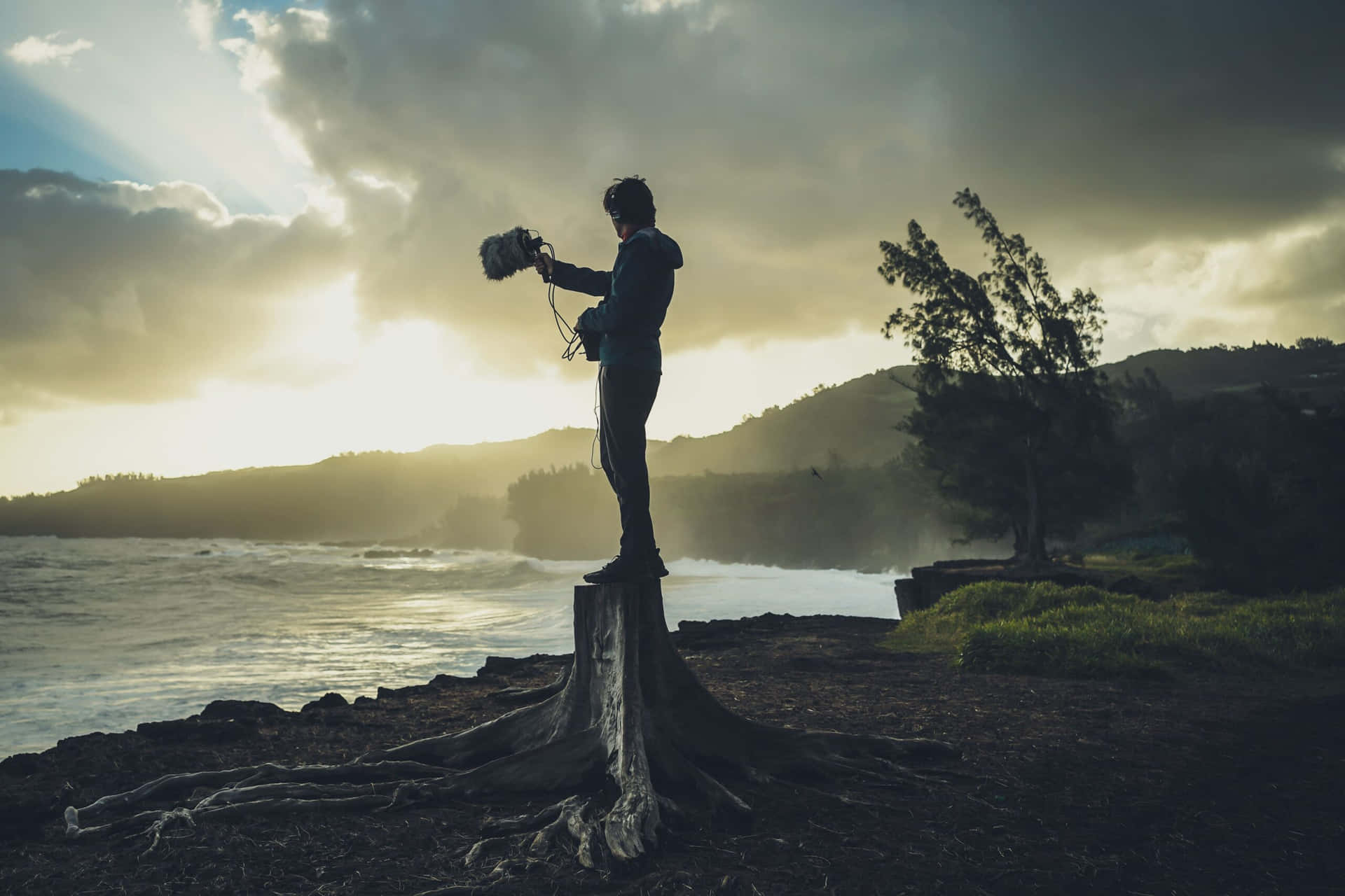 A Man Standing On A Tree Stump In Front Of The Ocean Background