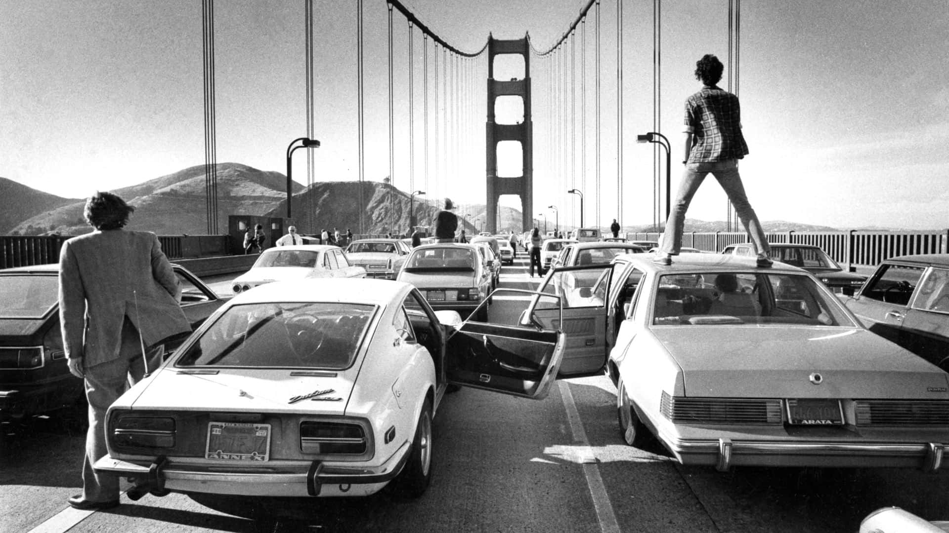 A Man Standing On Top Of A Car On The Golden Gate Bridge