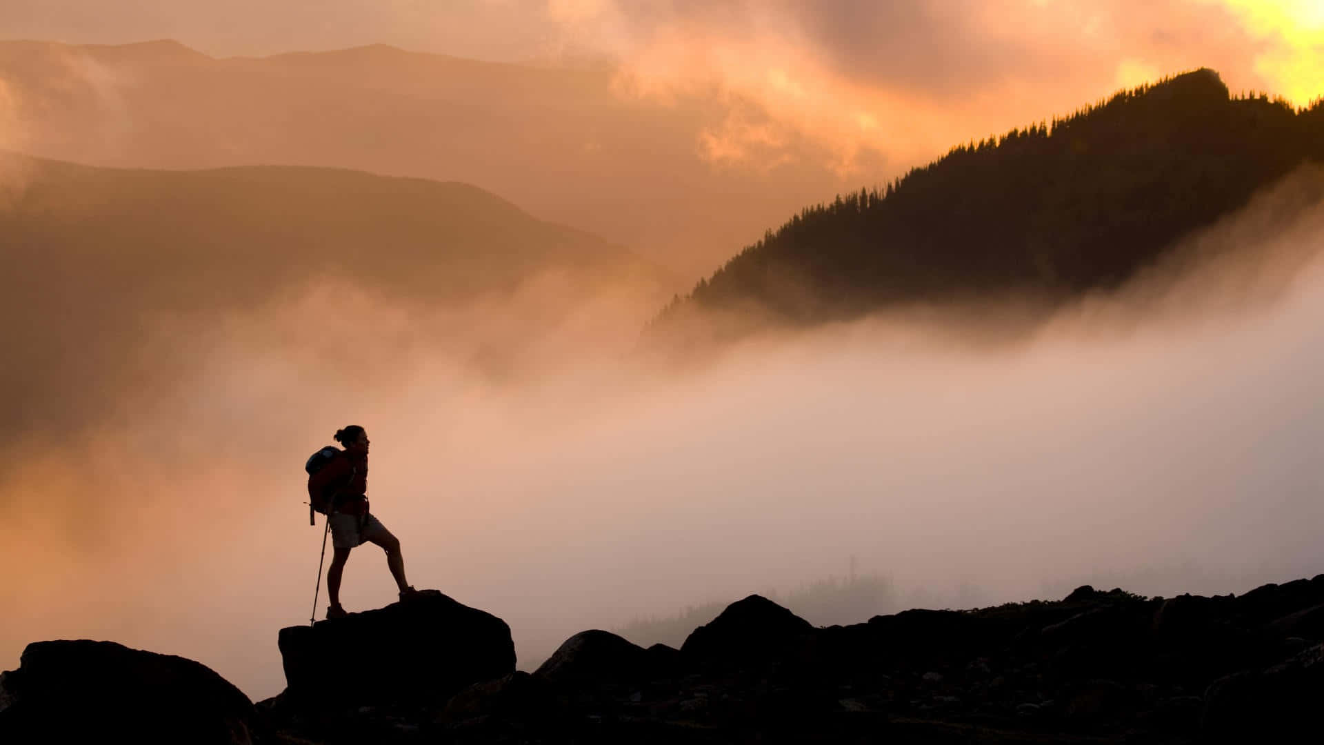 A Man Standing On Top Of Rocks In The Mountains At Sunset