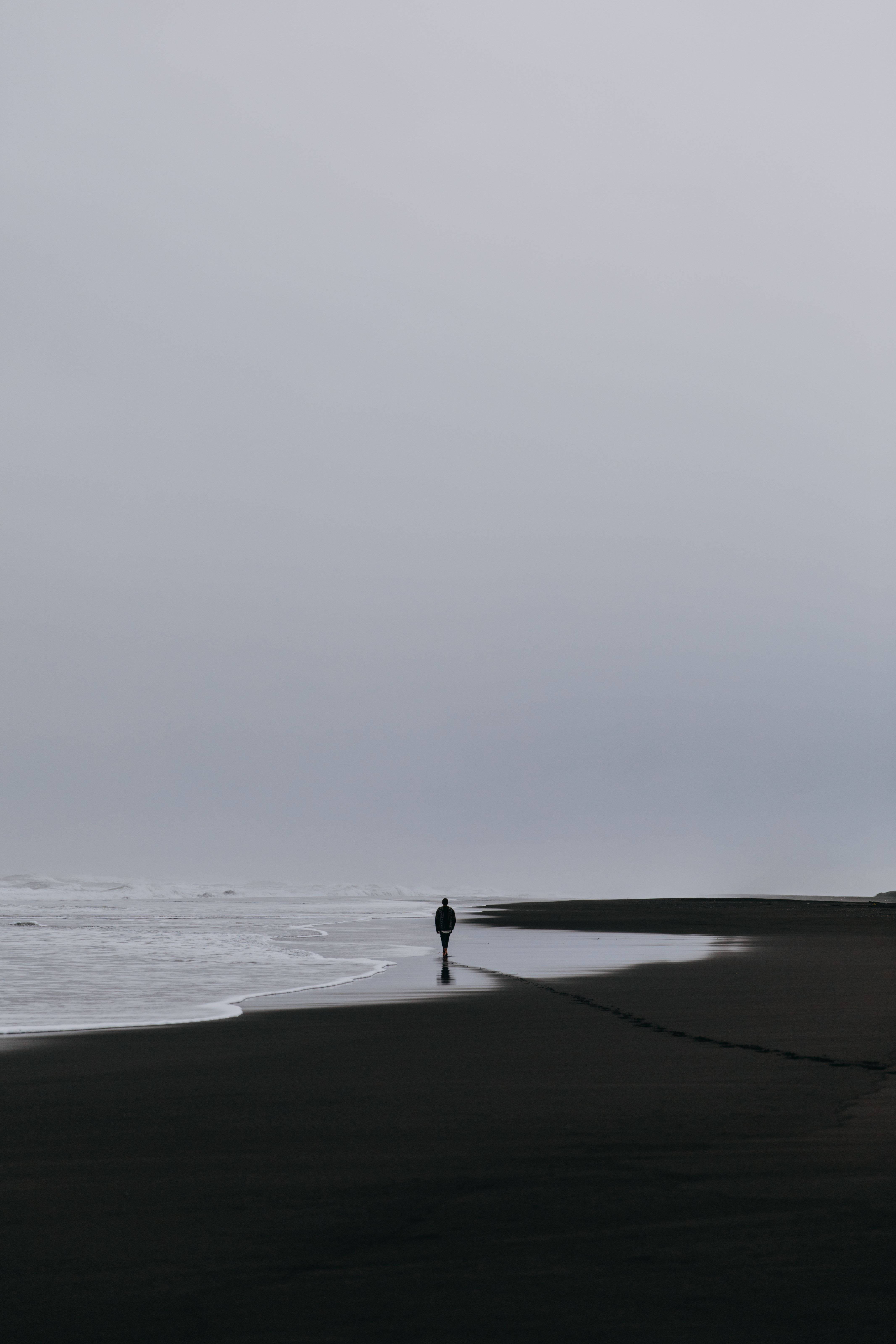 A Man Walking Alone On The Beach With His Phone Background