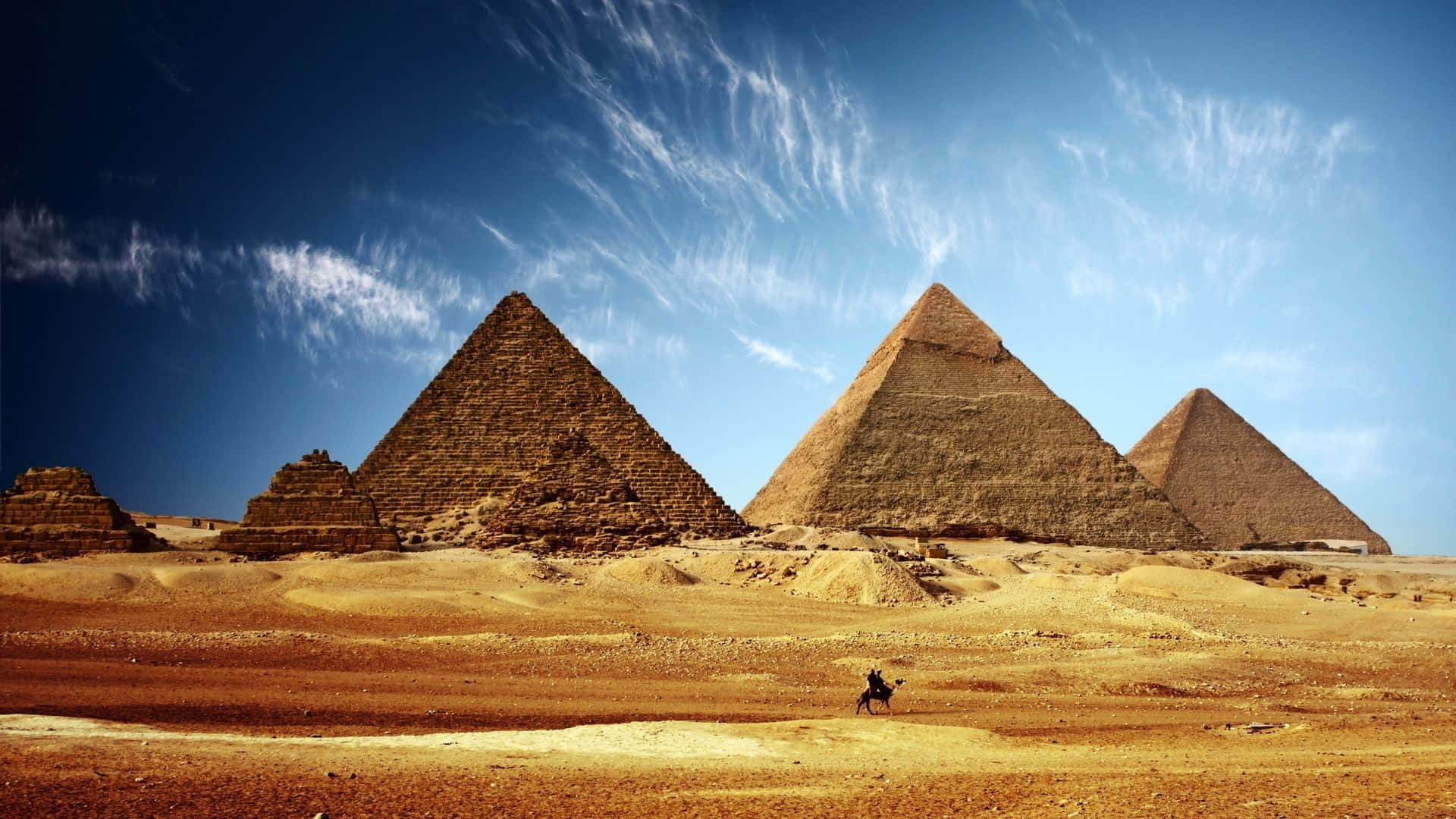 A Man Walks Through The Desert With The Pyramids In The Background