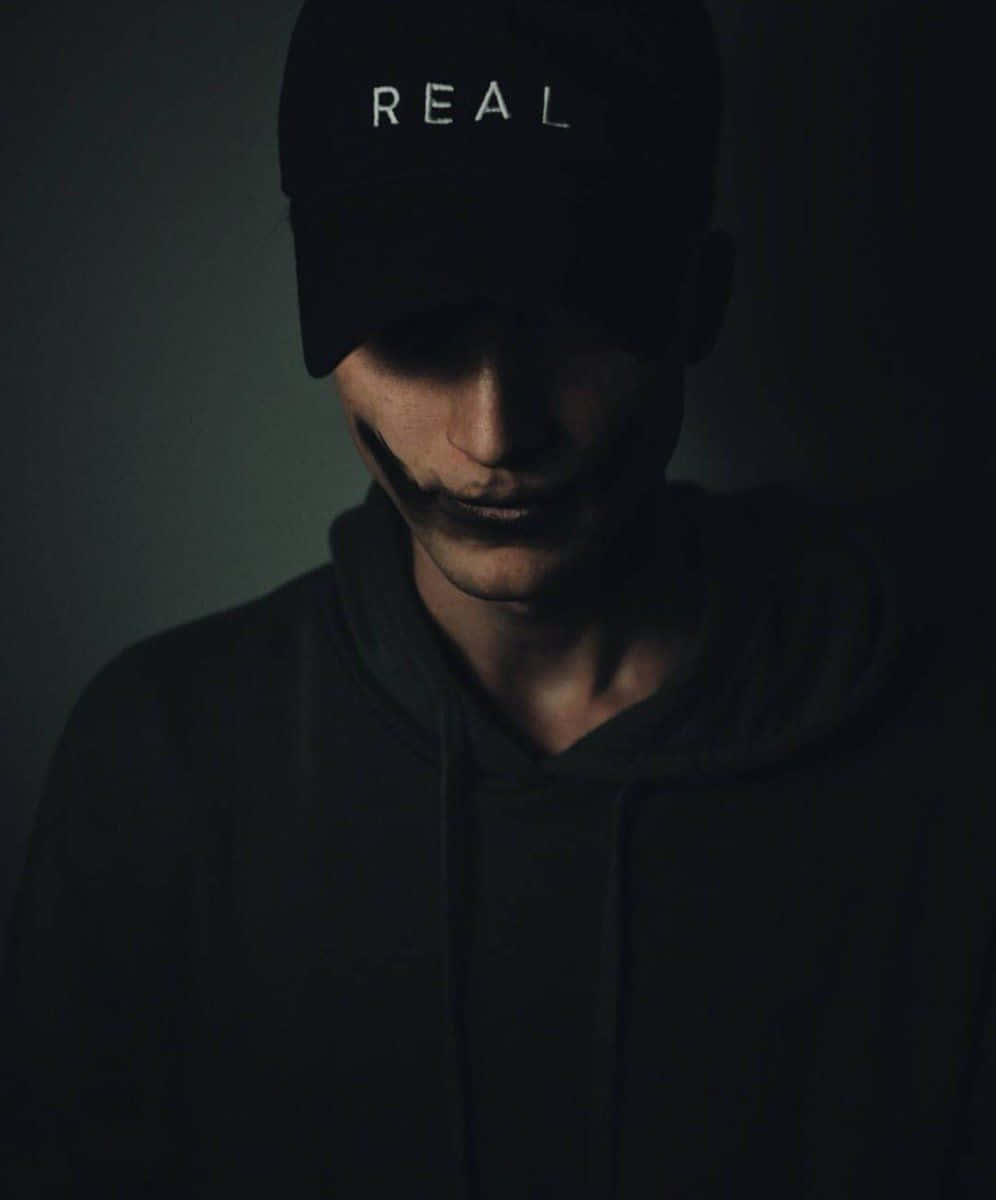 A Man Wearing A Black Baseball Cap With The Word Real On It Background