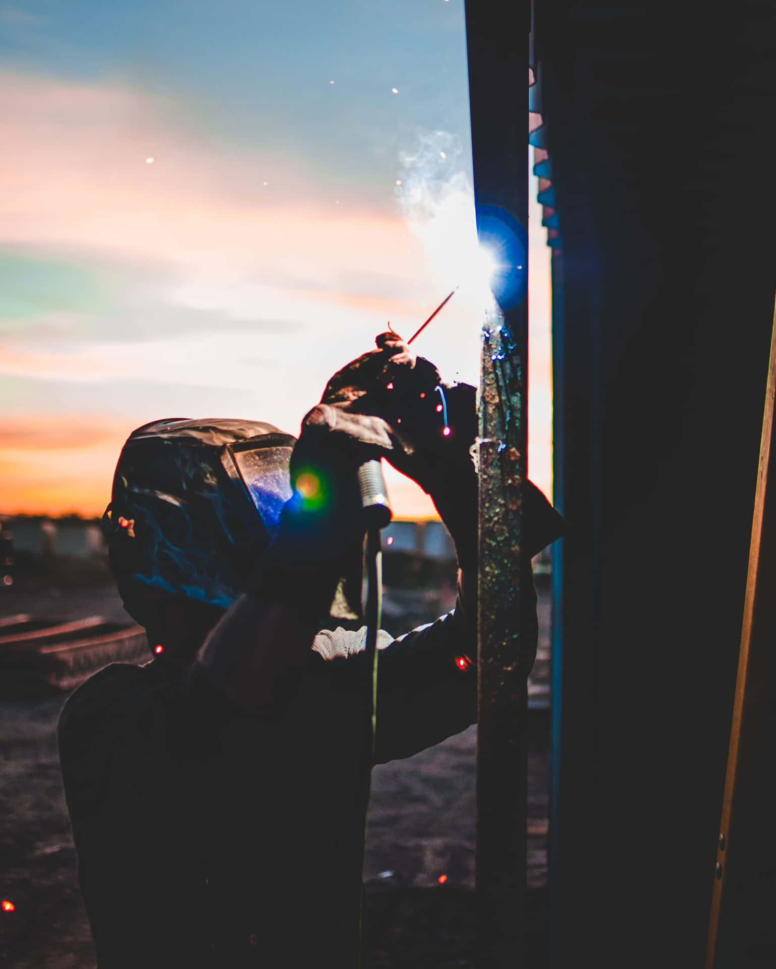 A Man Welding At Sunset Background