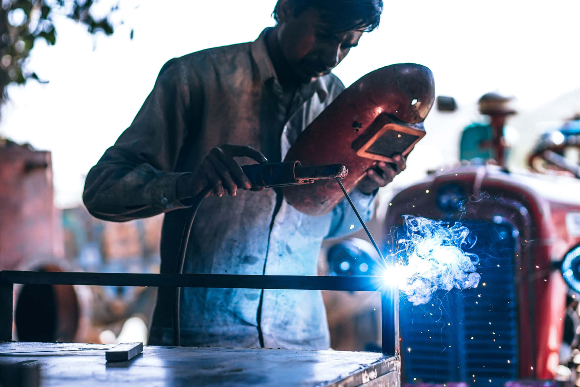 A Man Welding Metal On A Tractor Background