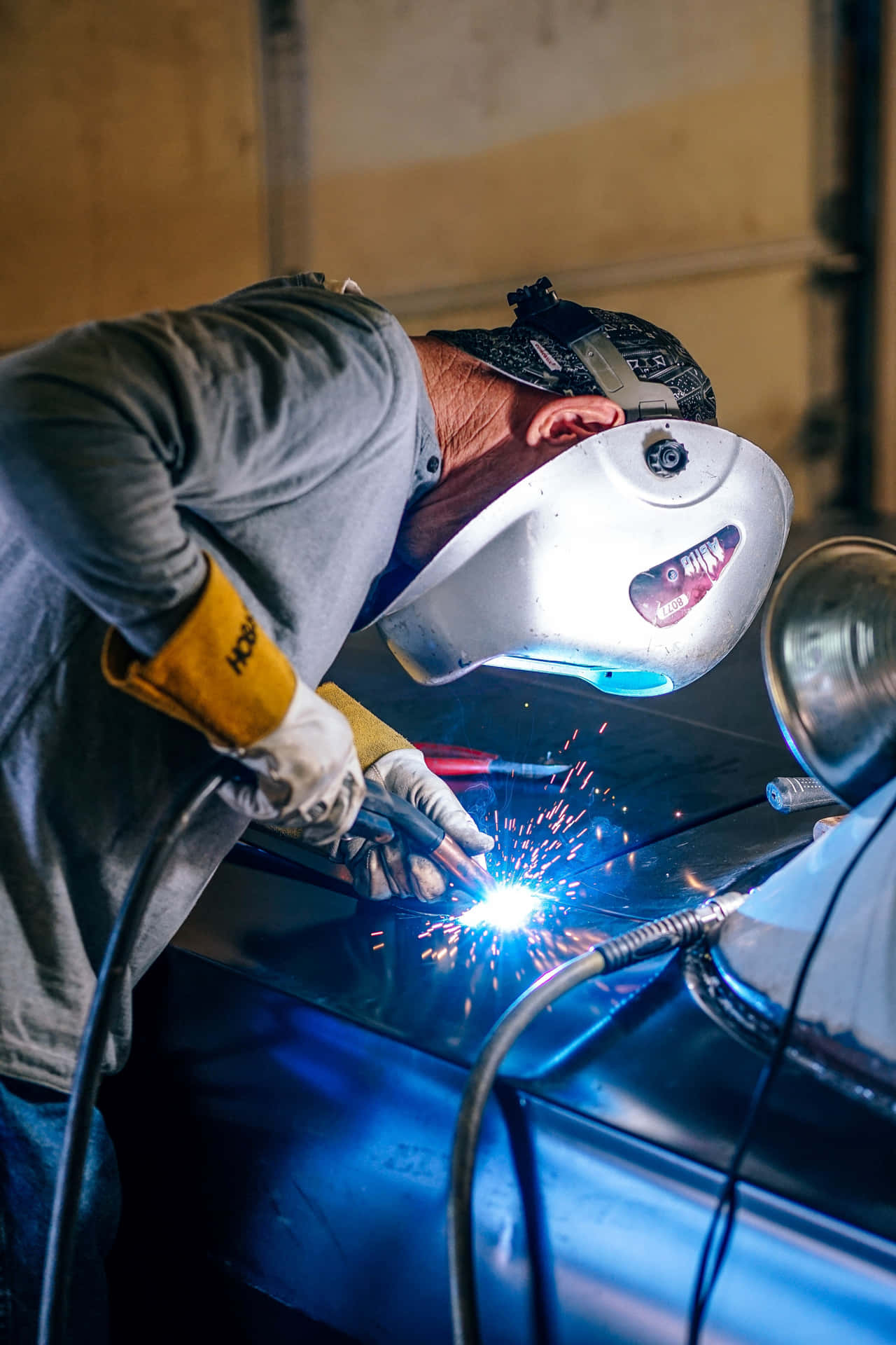 A Man Welding On A Blue Car Background