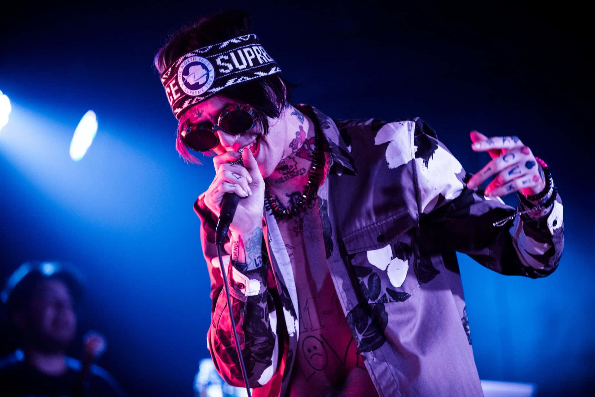 A Man With A Beanie And Sunglasses On Stage Background