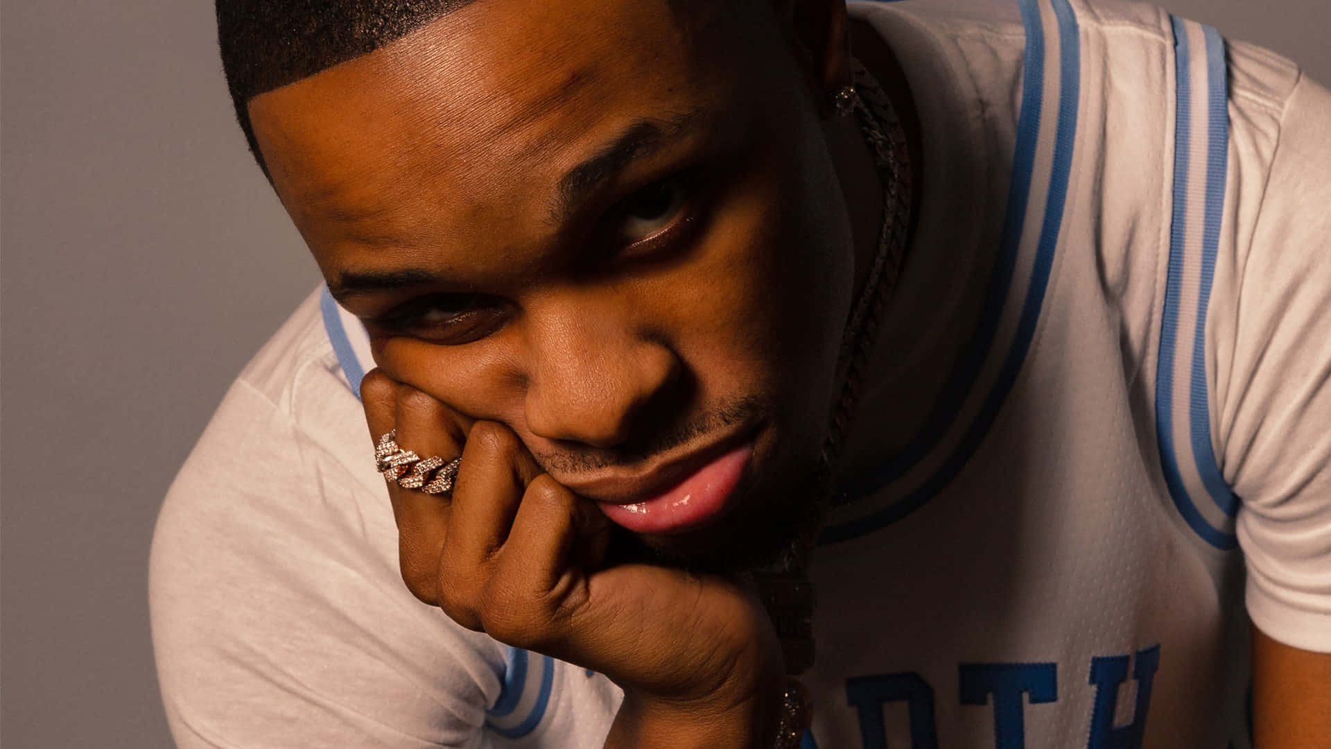 A Man With A Blue And White Shirt Is Posing With His Hand On His Chin Background