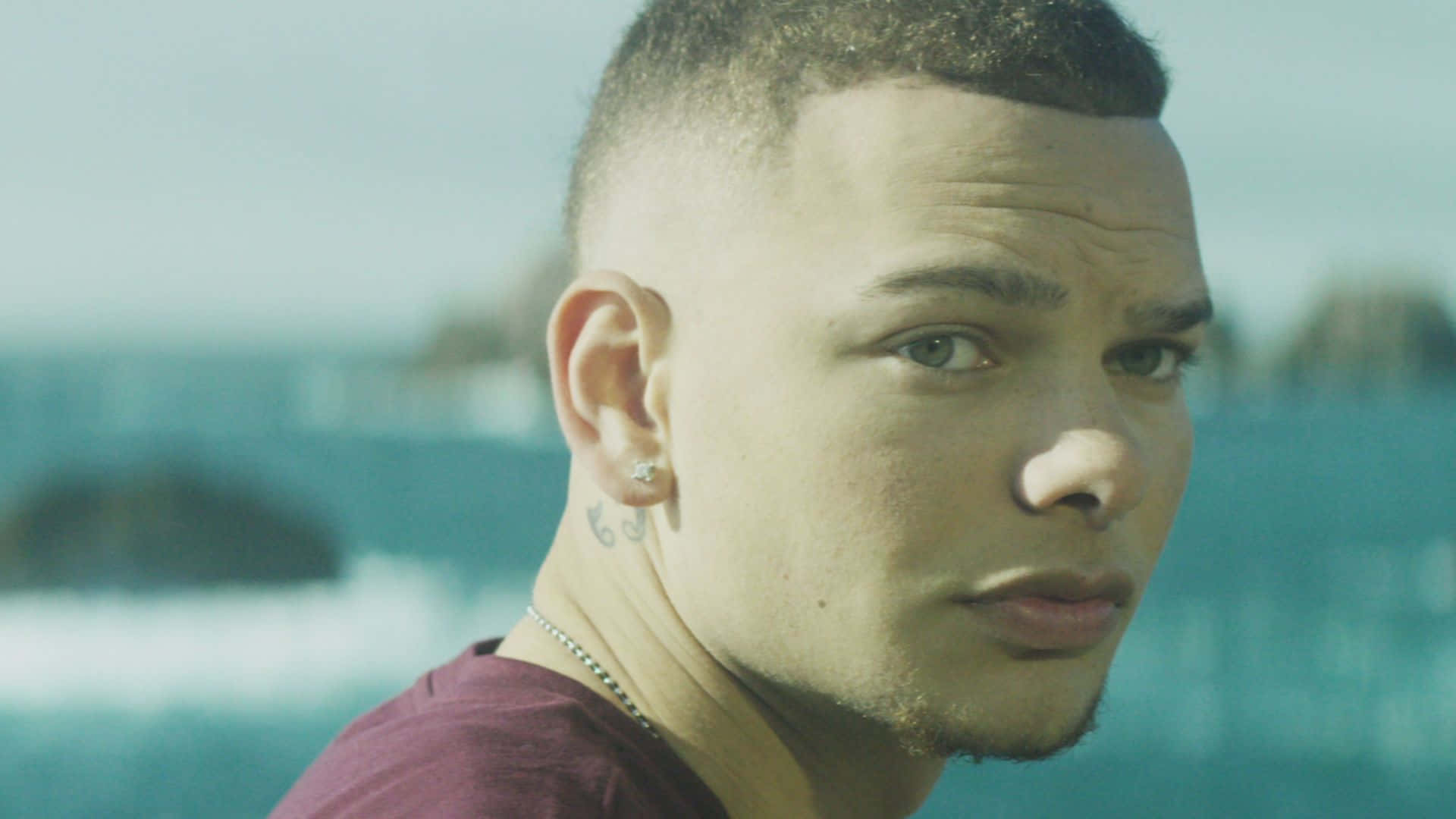 A Man With A Pierced Ear Is Looking At The Ocean Background