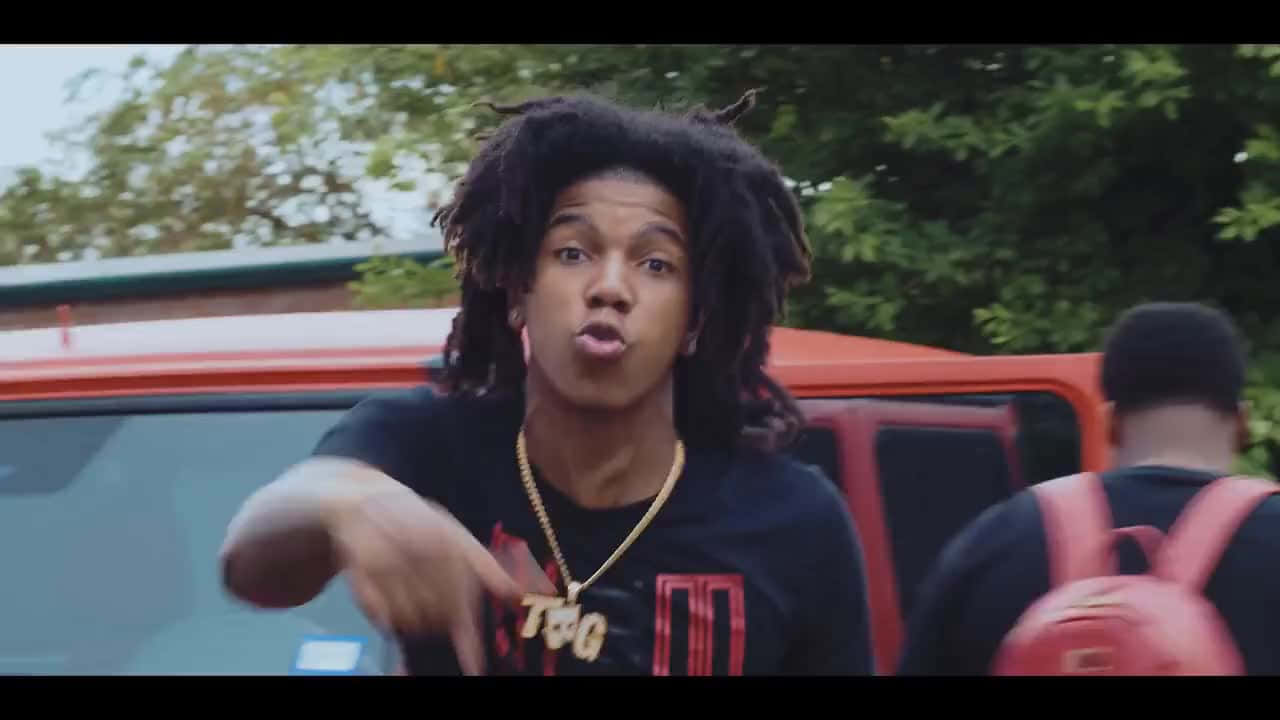 A Man With Dreadlocks Is Pointing At A Truck Background