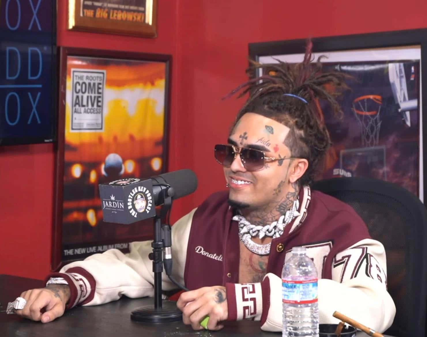 A Man With Dreadlocks Sitting In Front Of A Microphone Background