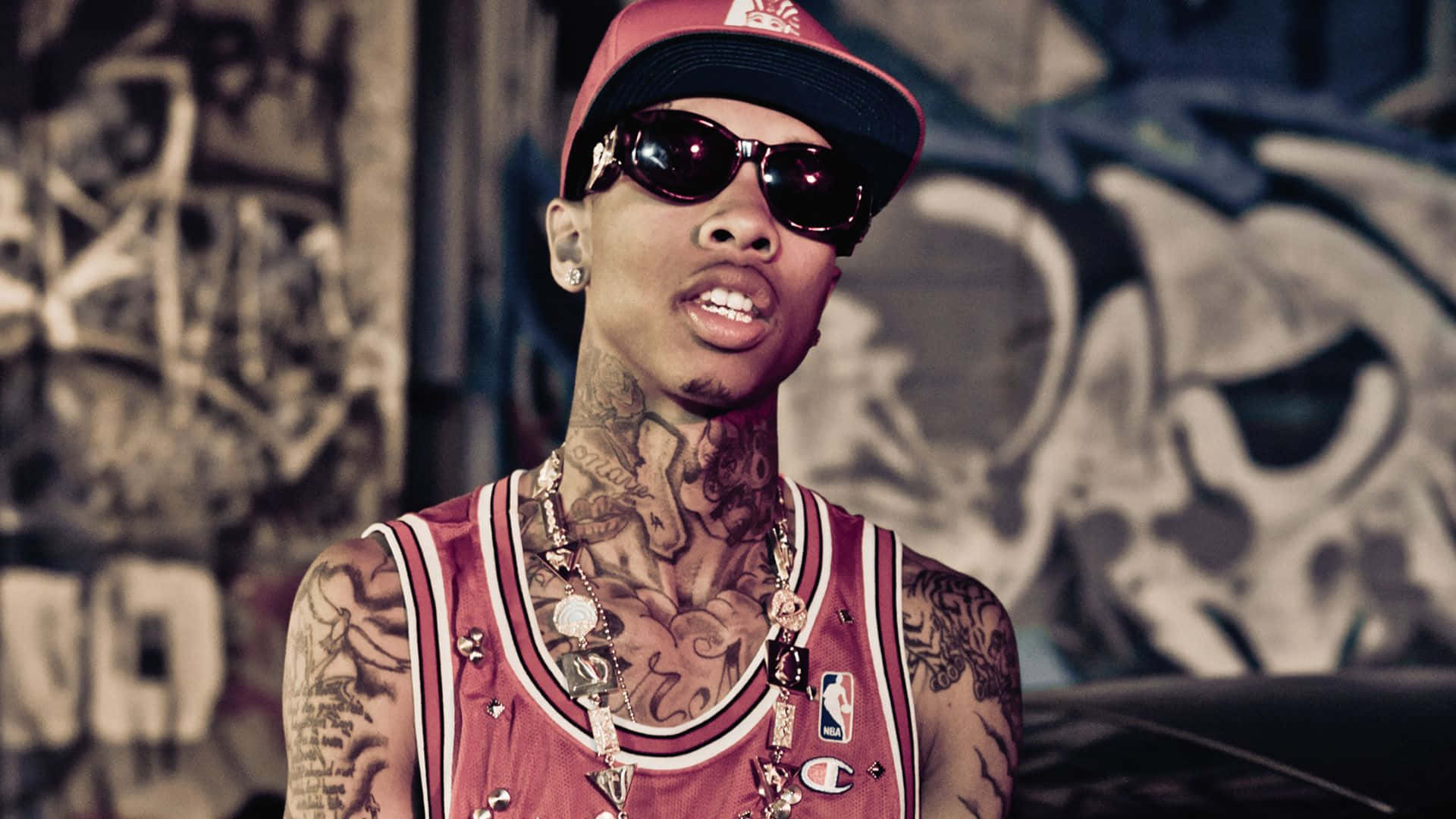 A Man With Tattoos And Sunglasses Standing In Front Of Graffiti Background