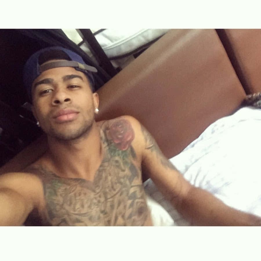 A Man With Tattoos Laying On A Bed Background