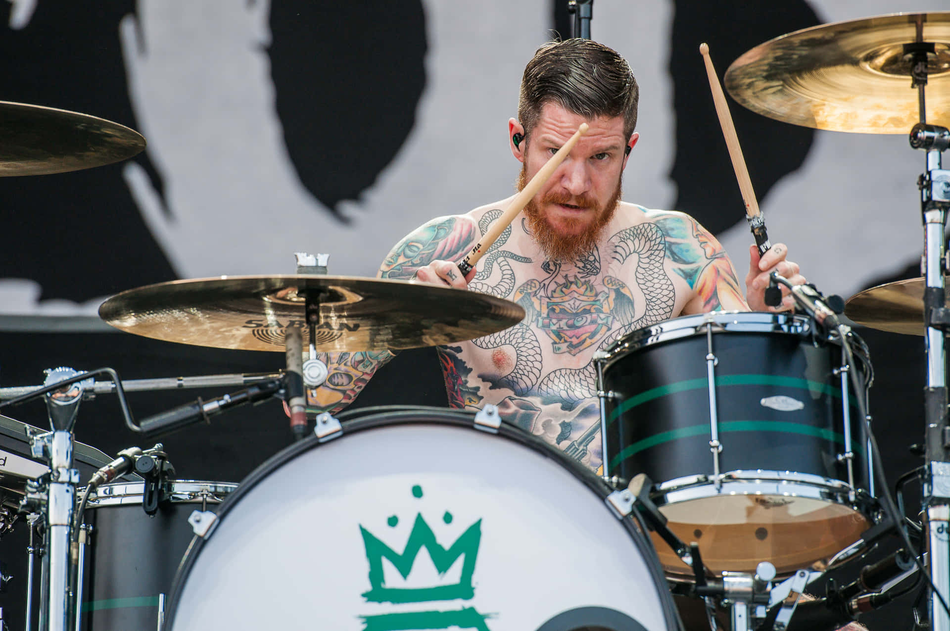 A Man With Tattoos Playing Drums On Stage Background