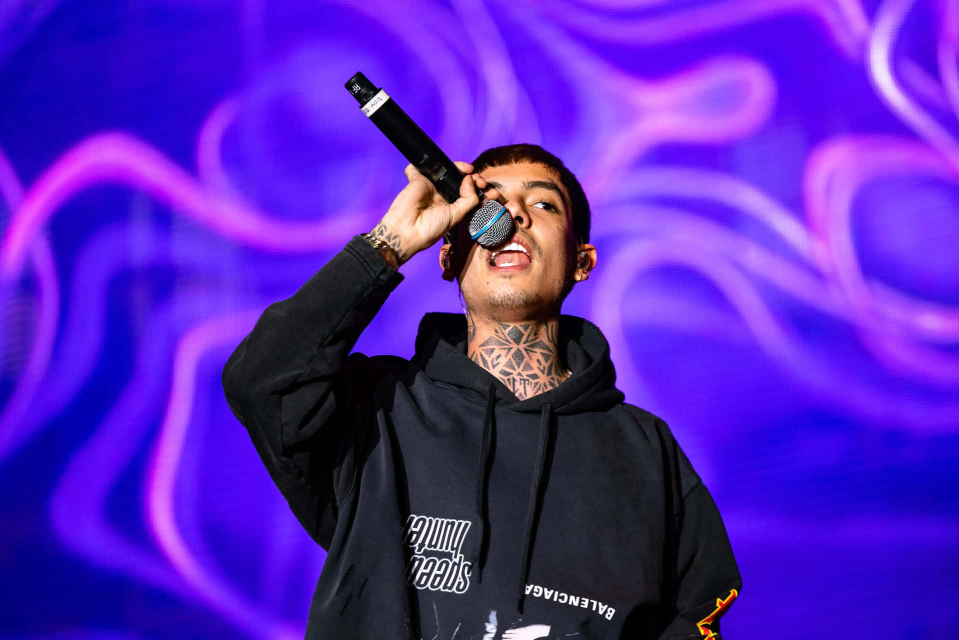 A Man With Tattoos Singing Into A Microphone Background