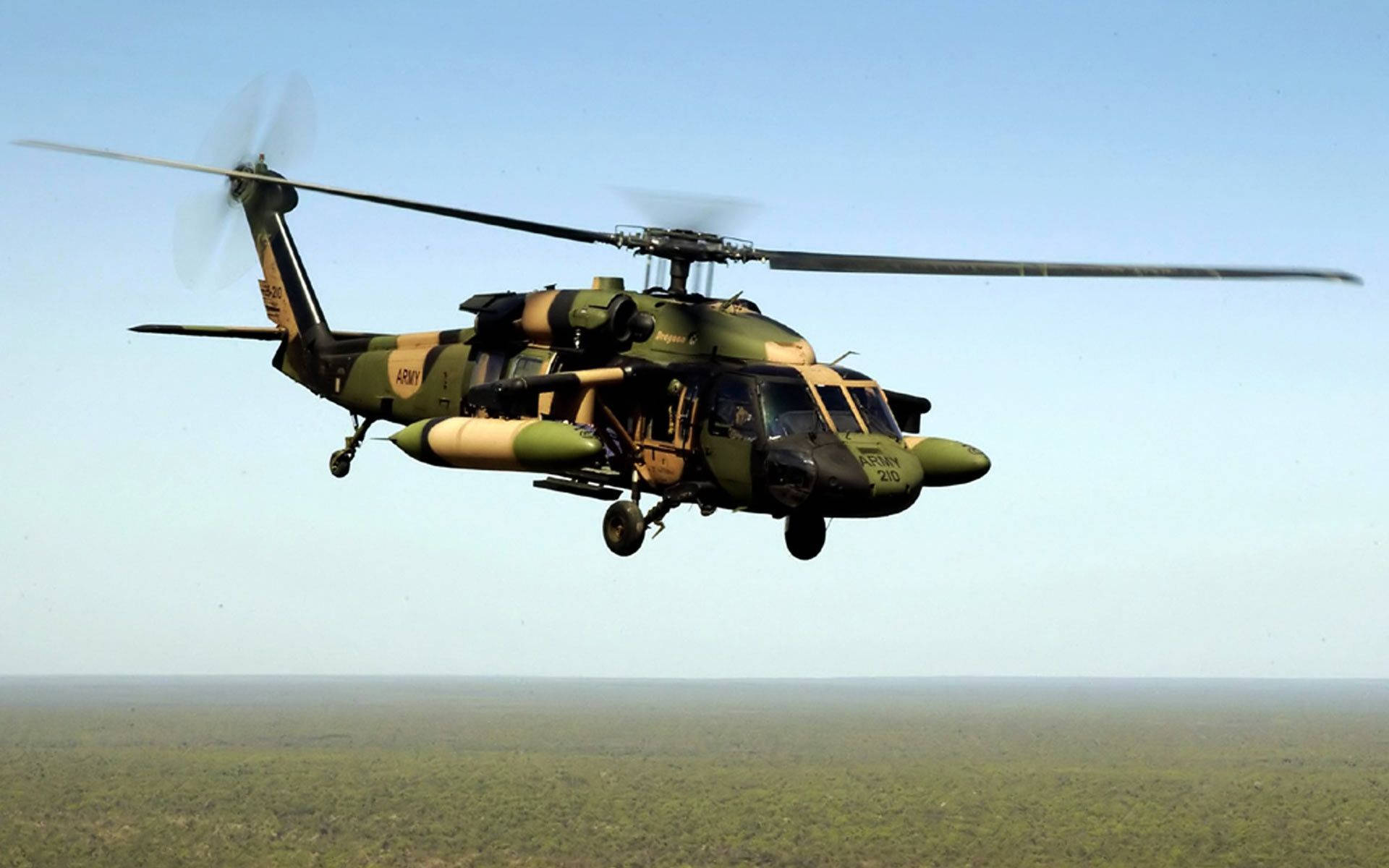 A Military Helicopter Flying Over A Forest Background