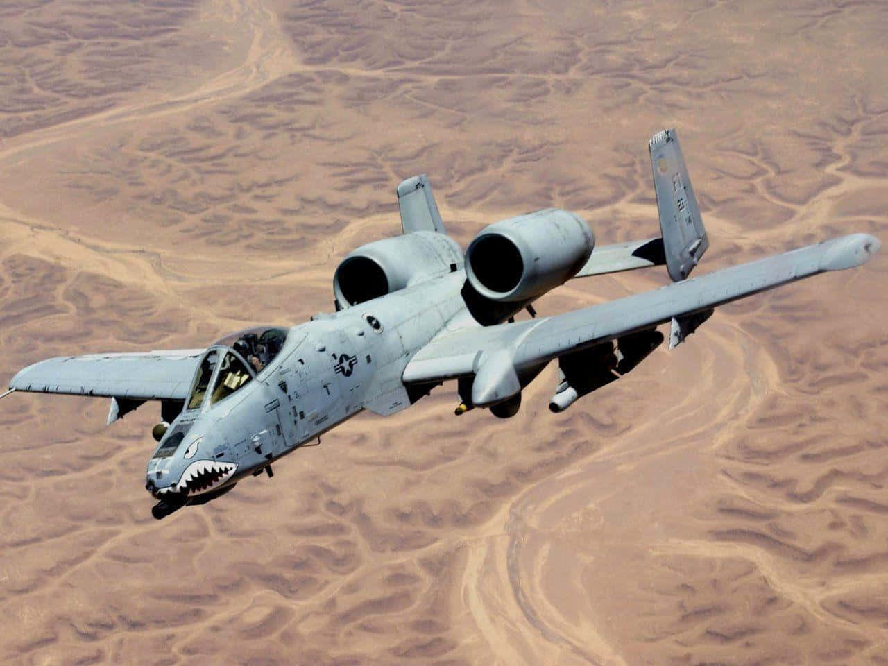 A Military Jet Flying Over A Desert Background