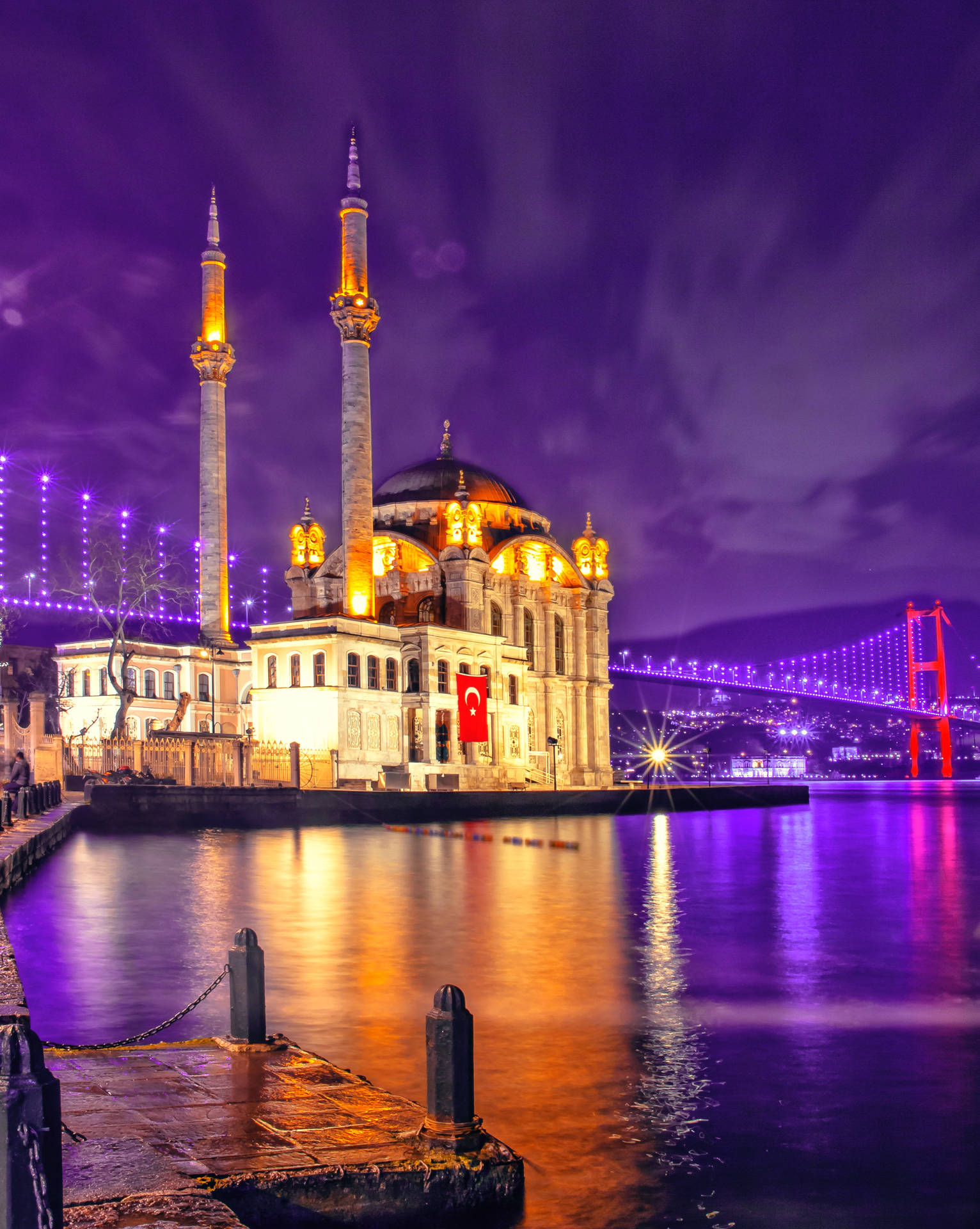 A Mosque Is Lit Up At Night With A Bridge Background