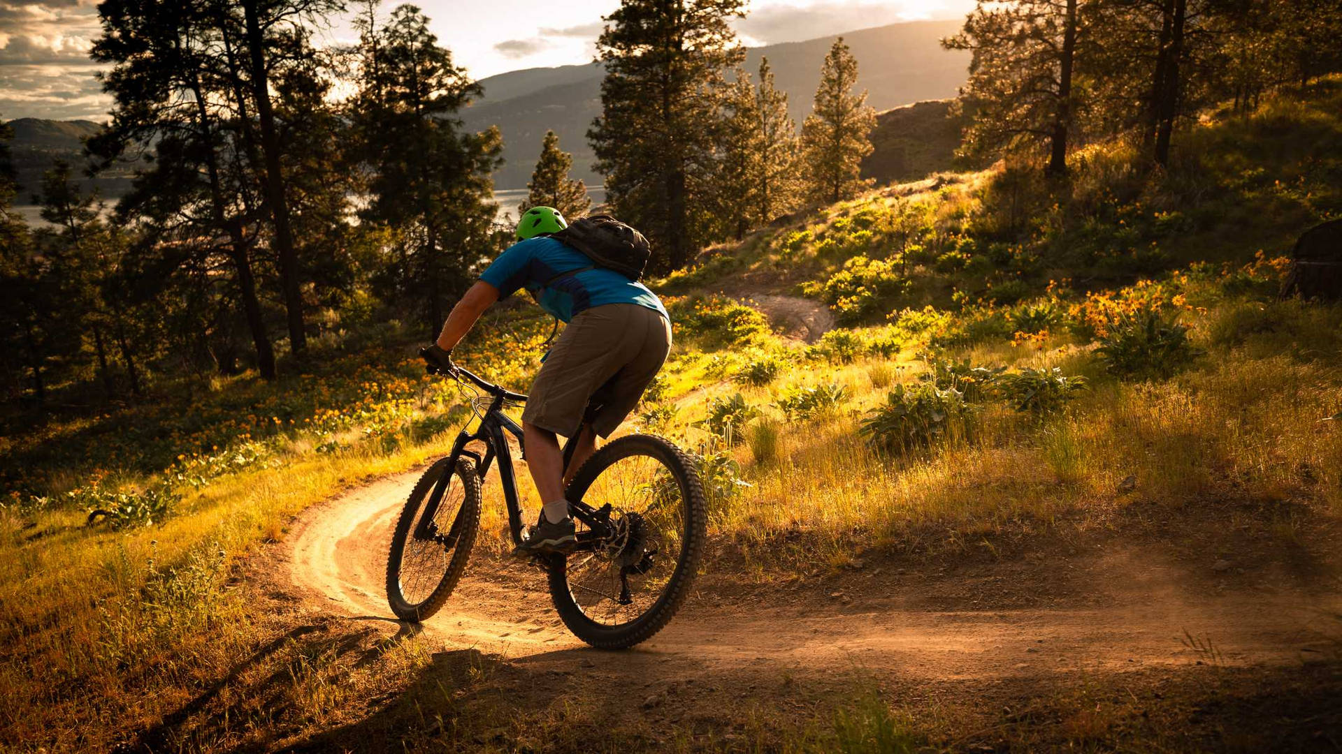 A Mountain Biker Racing Downhill Against The Backdrop Of A Breath-taking Sunset. Background