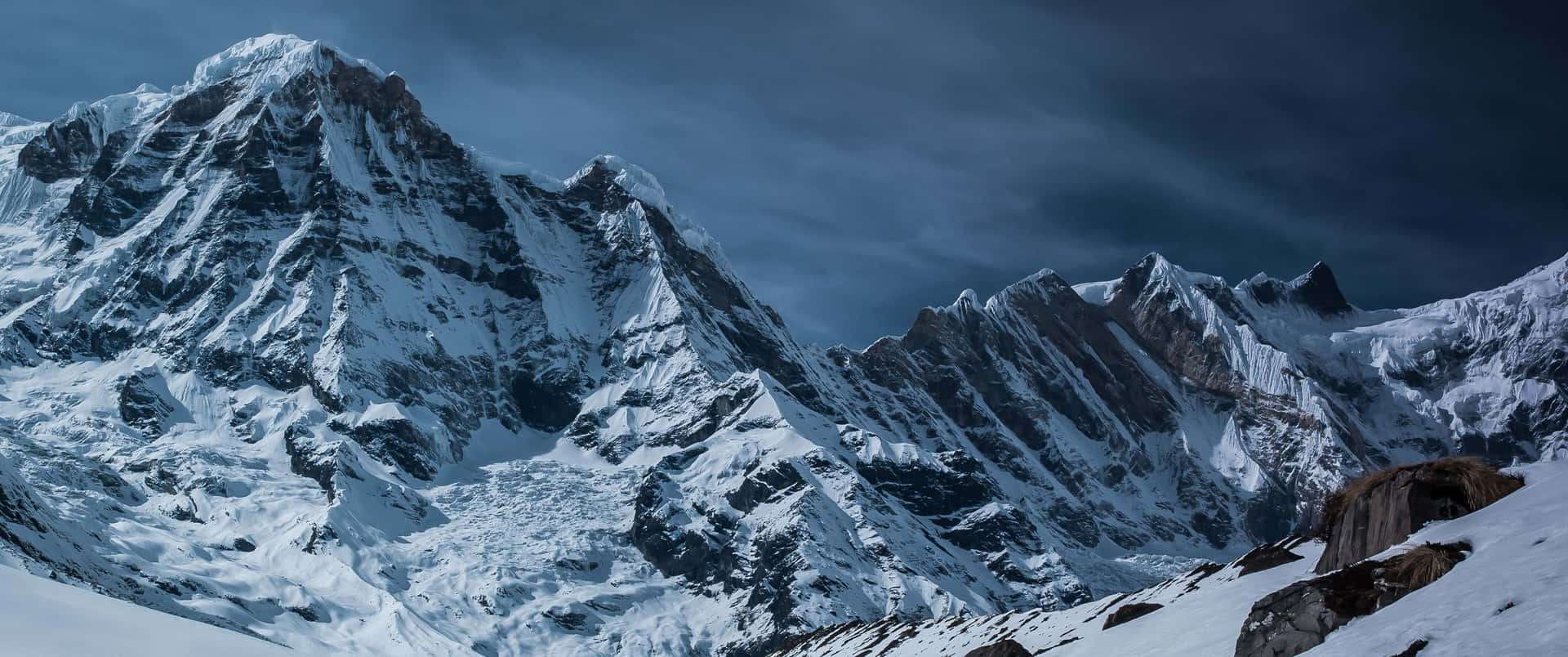 A Mountain Covered In Snow With A Cloudy Sky Background
