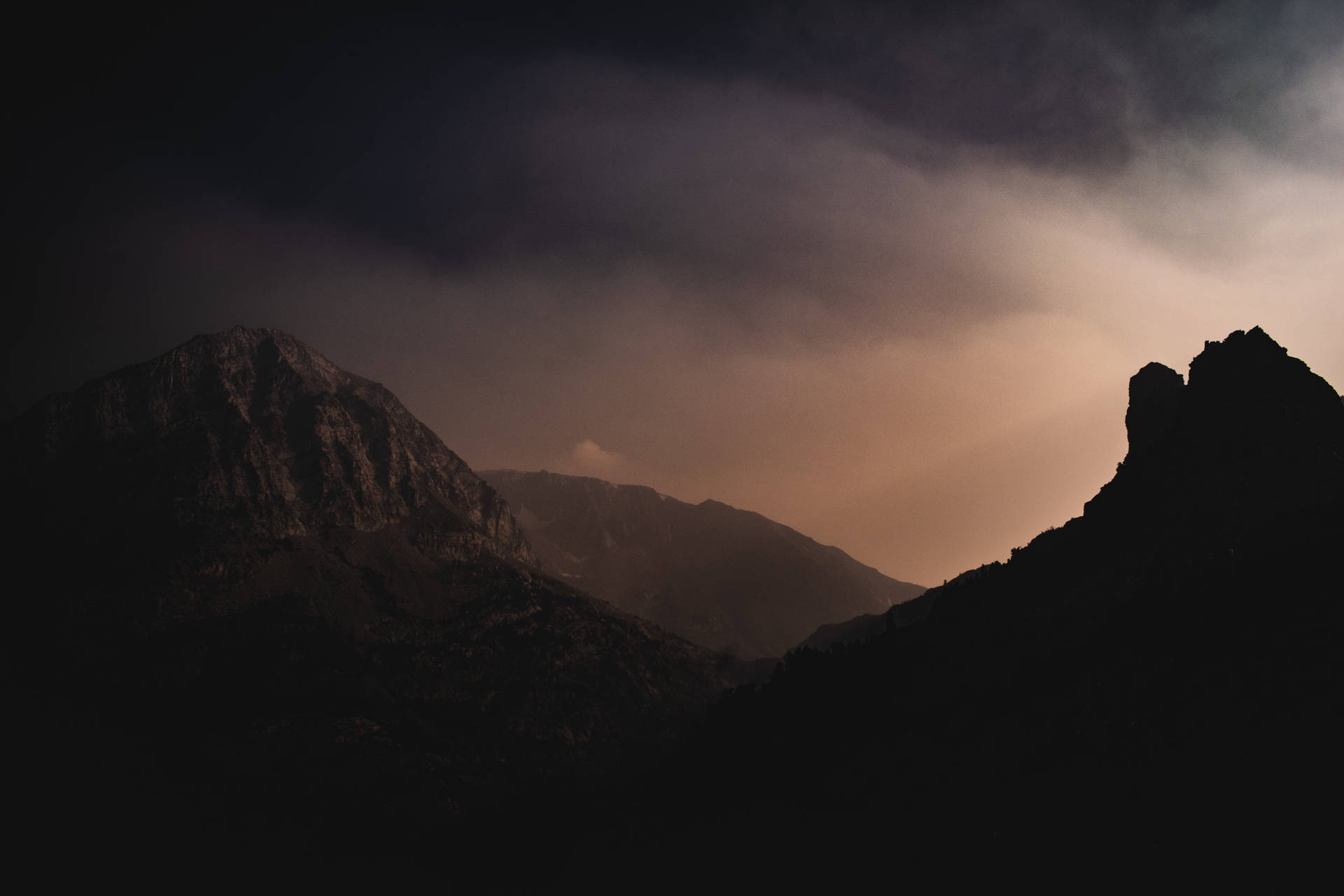 A Mountain Range With A Sun Shining Through The Clouds