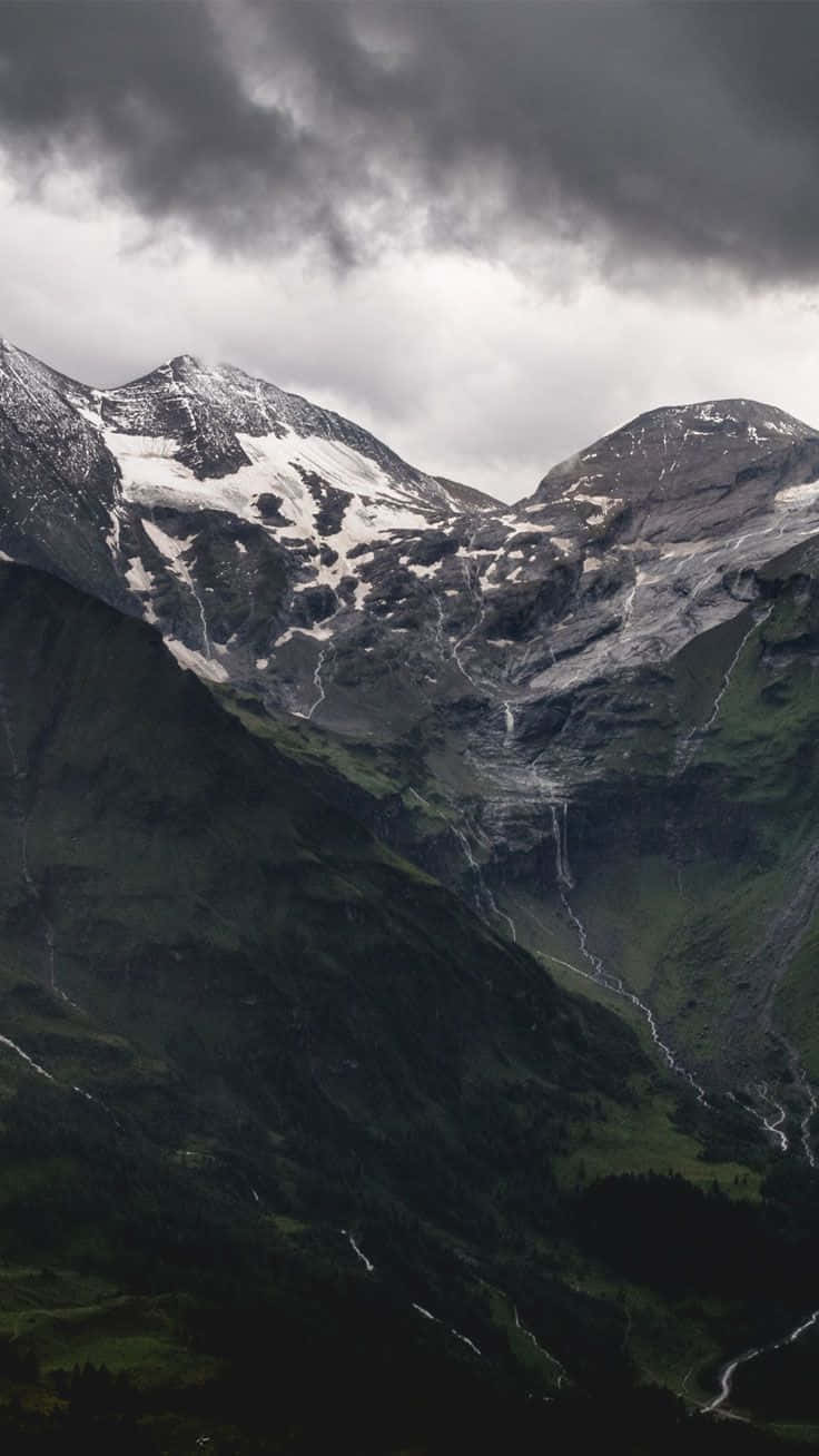 A Mountain Range With Snow Covered Mountains Under A Cloudy Sky Background