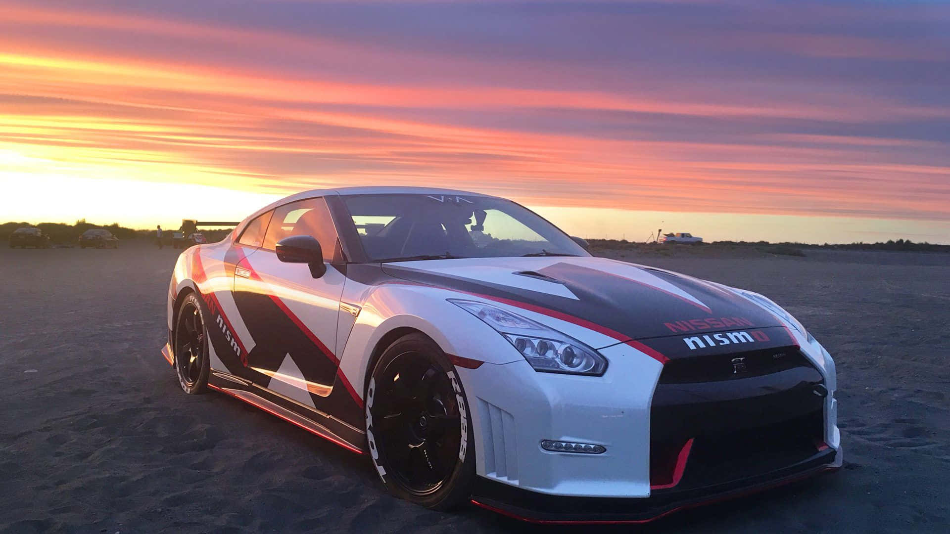 A Nissan Gtr Parked On The Beach At Sunset Background