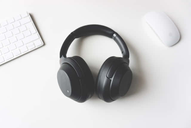 A Pair Of Headphones On A Desk Next To A Keyboard Background
