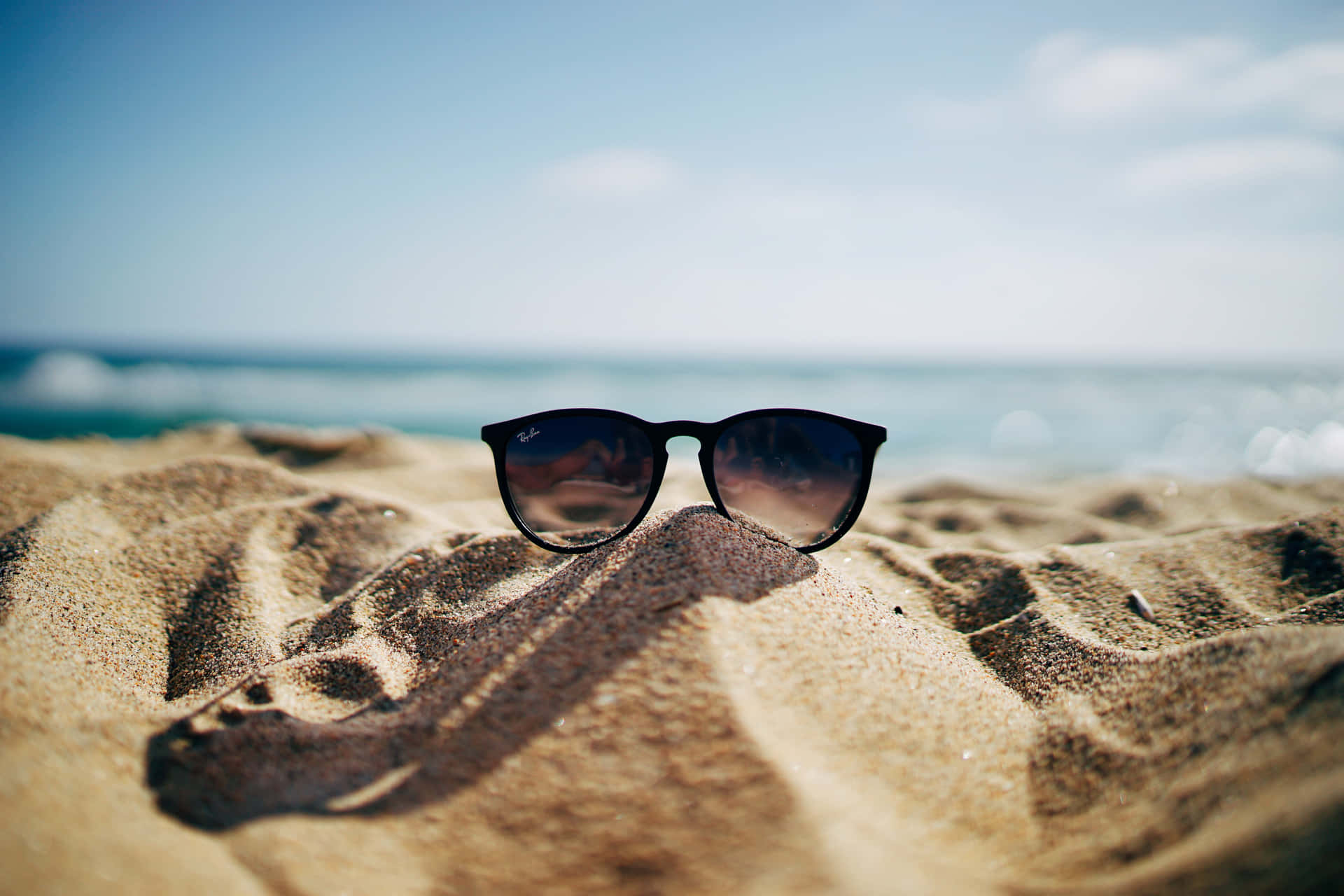 A Pair Of Sunglasses On The Sand Background