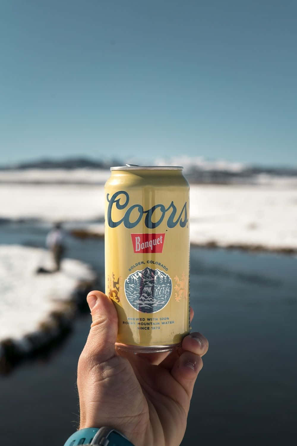 A Person Holding A Can Of Coors Light In Front Of A River Background