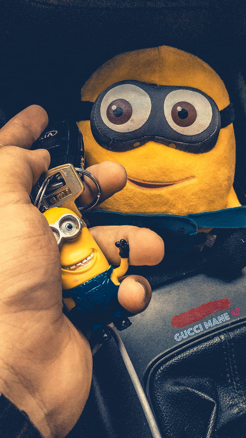 A Person Holding A Minion Keychain Background