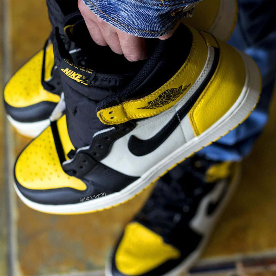 A Person Holding A Pair Of Yellow And Black Air Jordan 1s Background