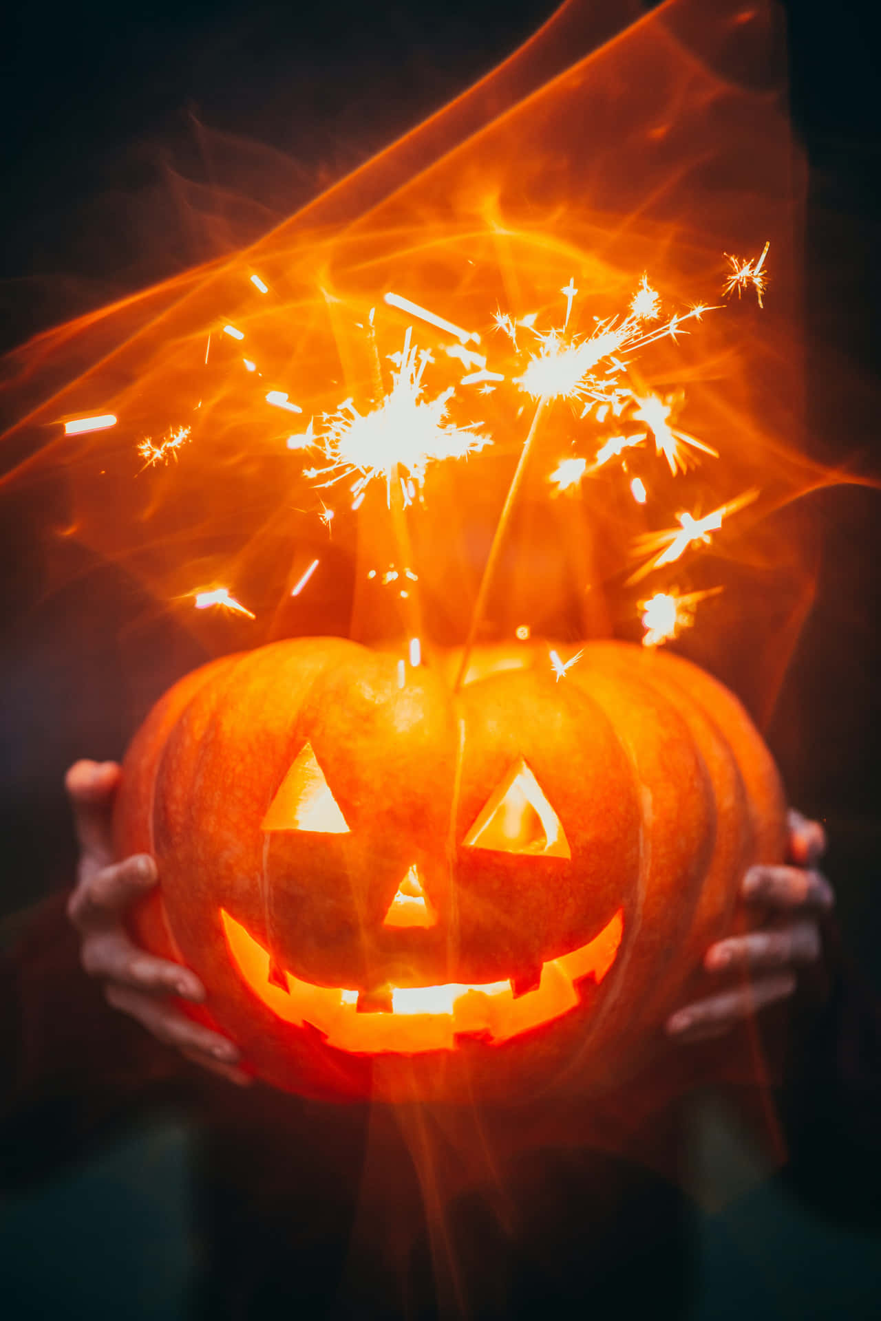 A Person Holding A Pumpkin With Sparklers In It Background