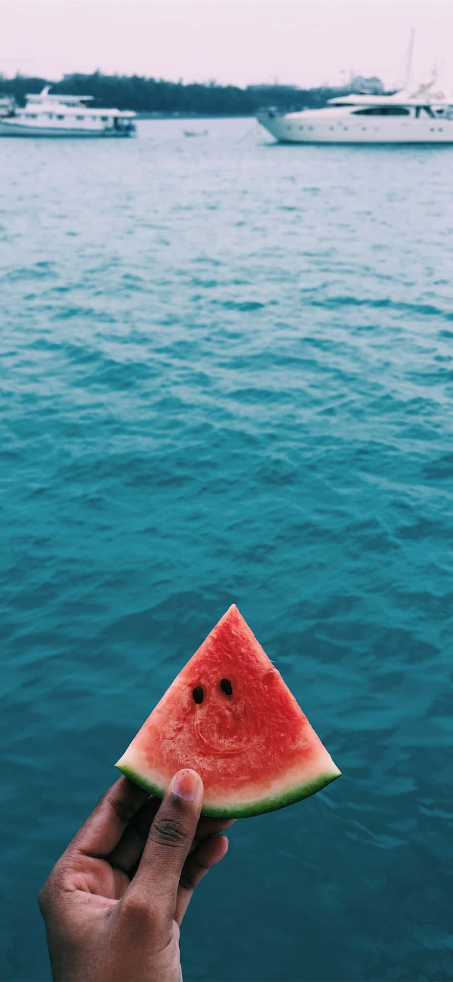 A Person Holding A Slice Of Watermelon In Front Of A Boat Background