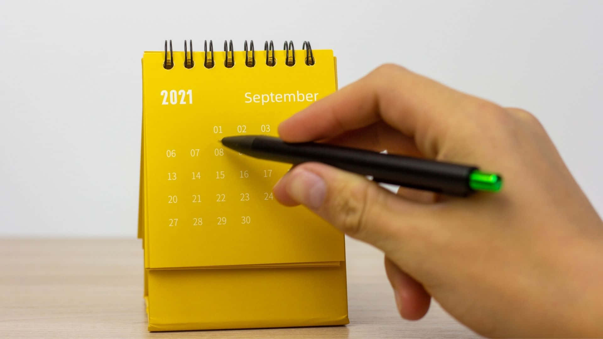 A Person Holding A Yellow Calendar With A Pen Background