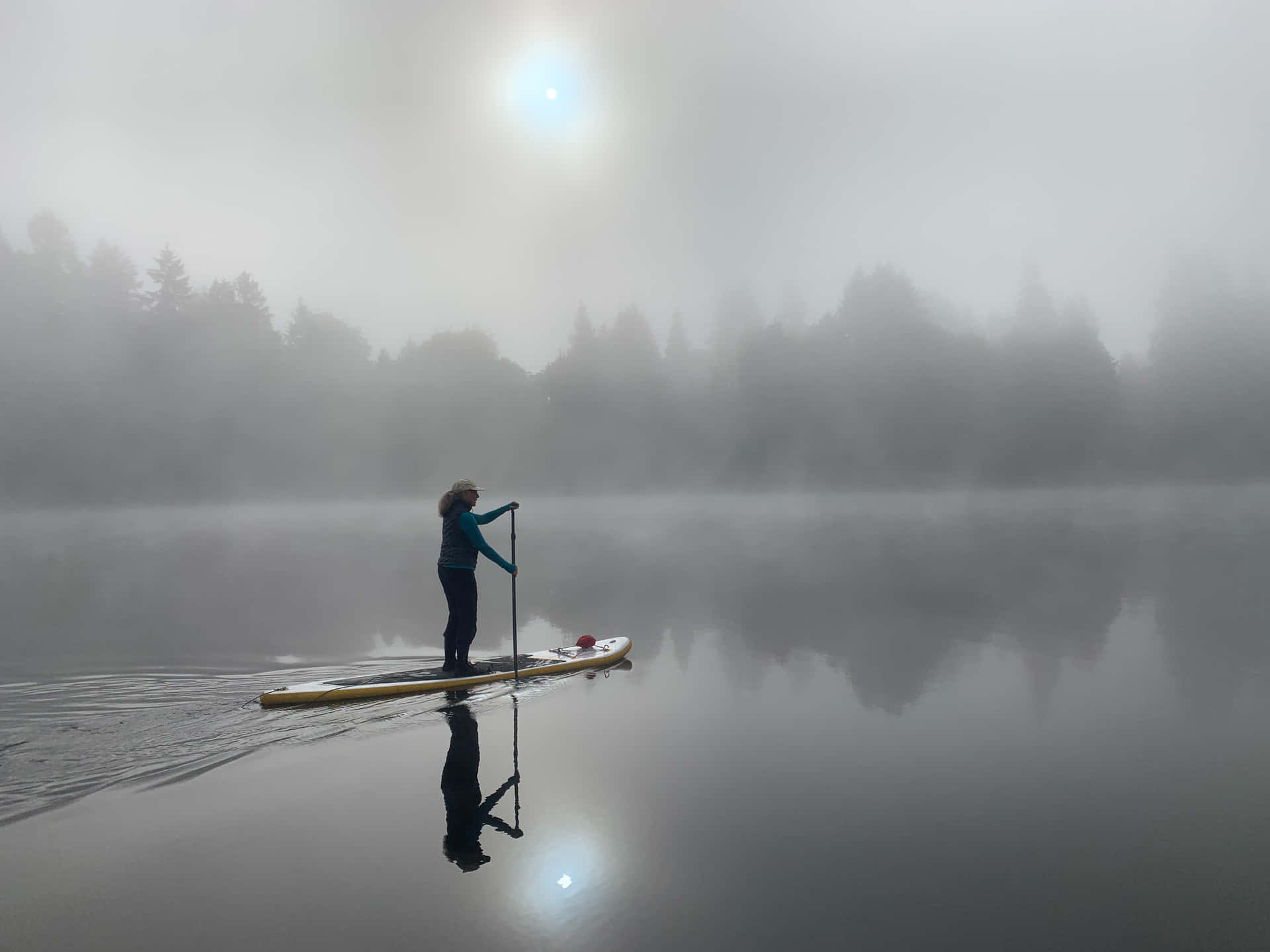 A Person Paddle Boarding In The Fog Background