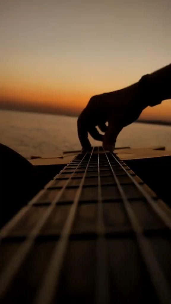 A Person Playing An Acoustic Guitar At Sunset Background