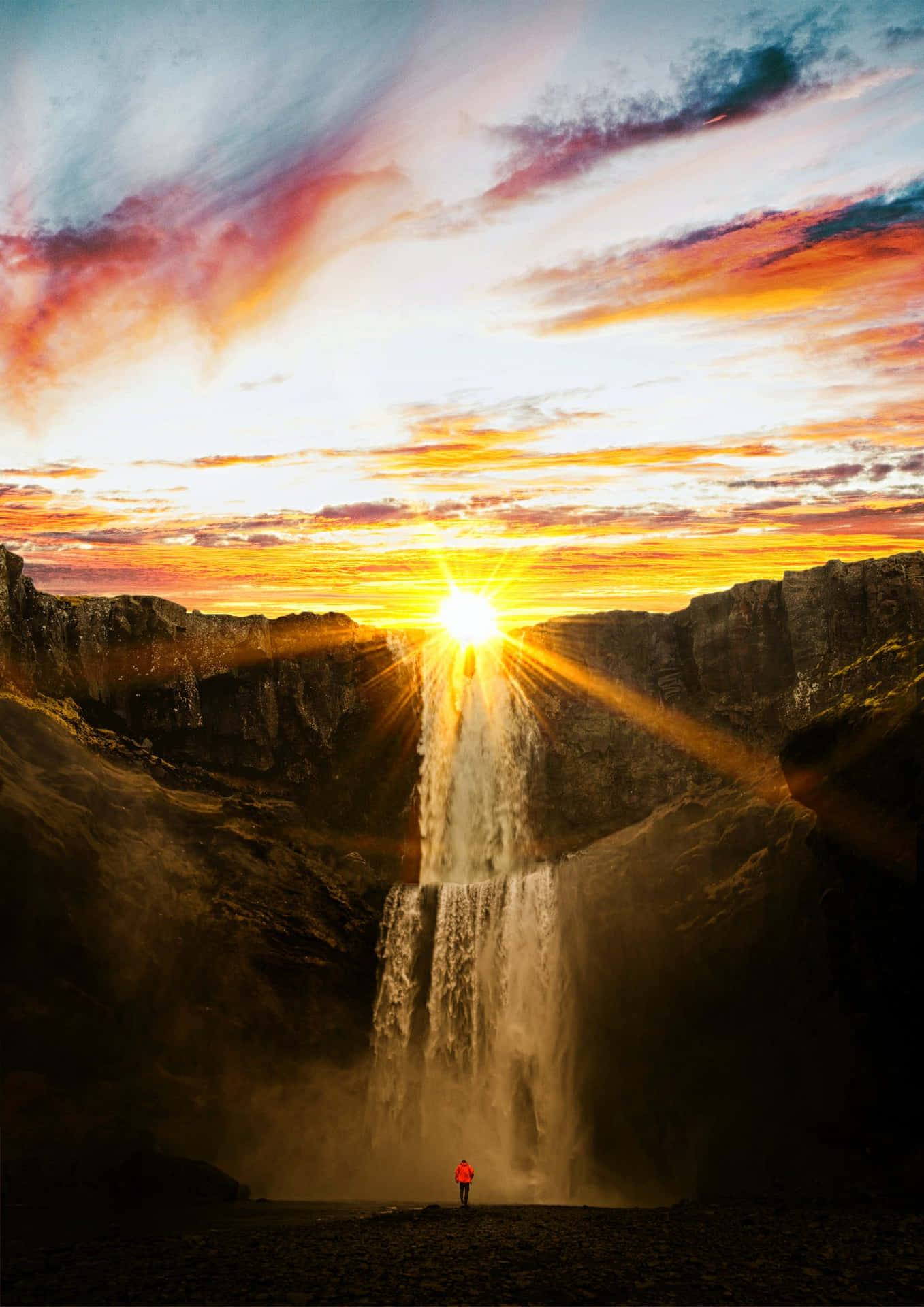 A Person Standing In Front Of A Waterfall At Sunset