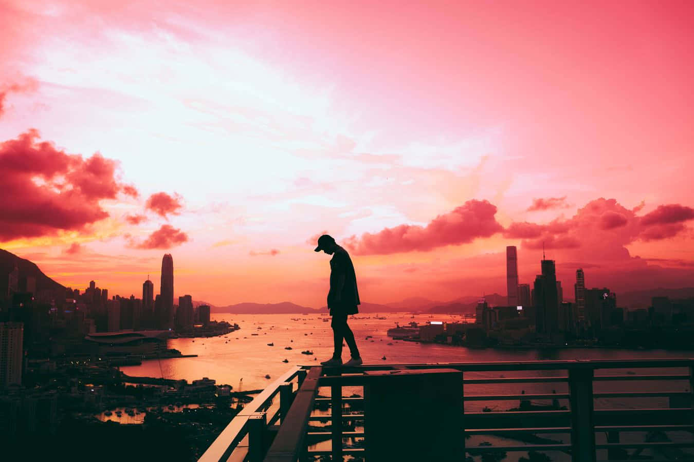 A Person Standing On A Ledge Overlooking A City At Sunset Background