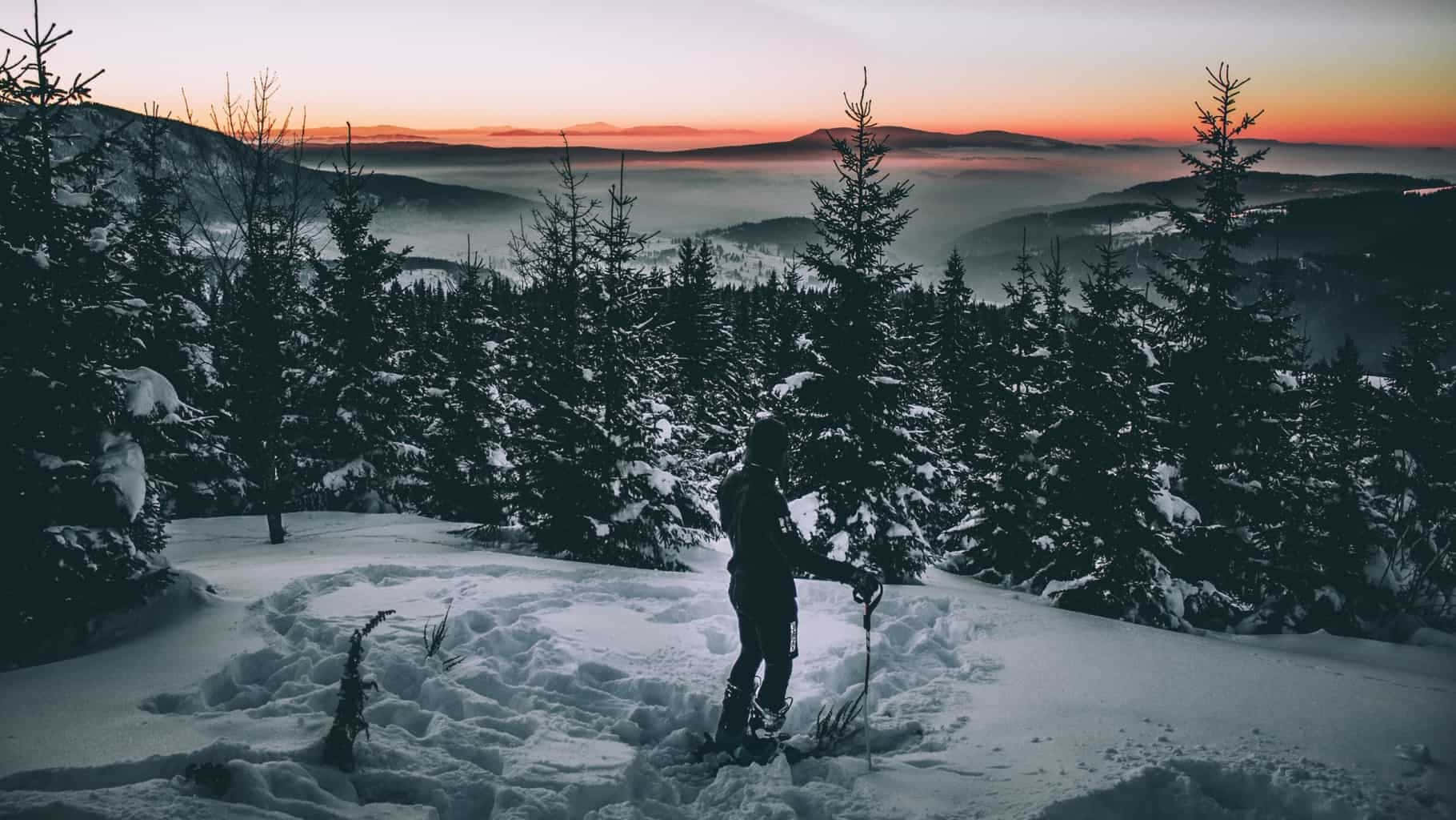 A Person Standing On A Snow Covered Mountain At Sunset Background
